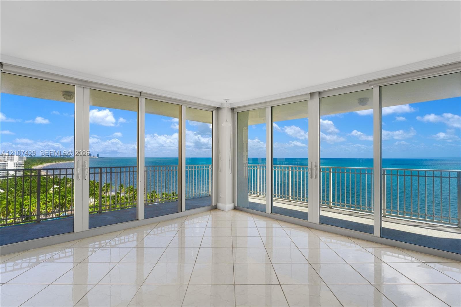 Floor-to-ceiling glass doors, expansive balcony with metal railing, polished tile flooring, and neutral wall finishes