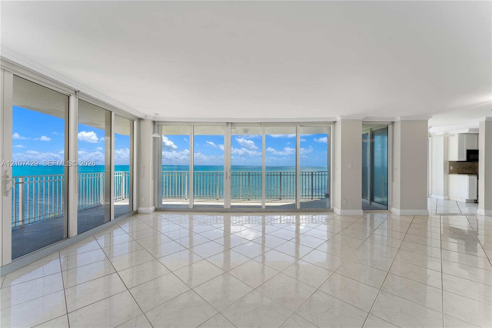 Expansive interior space featuring large-format tile flooring, crown molding, and floor-to-ceiling glass panel walls with access to a balcony