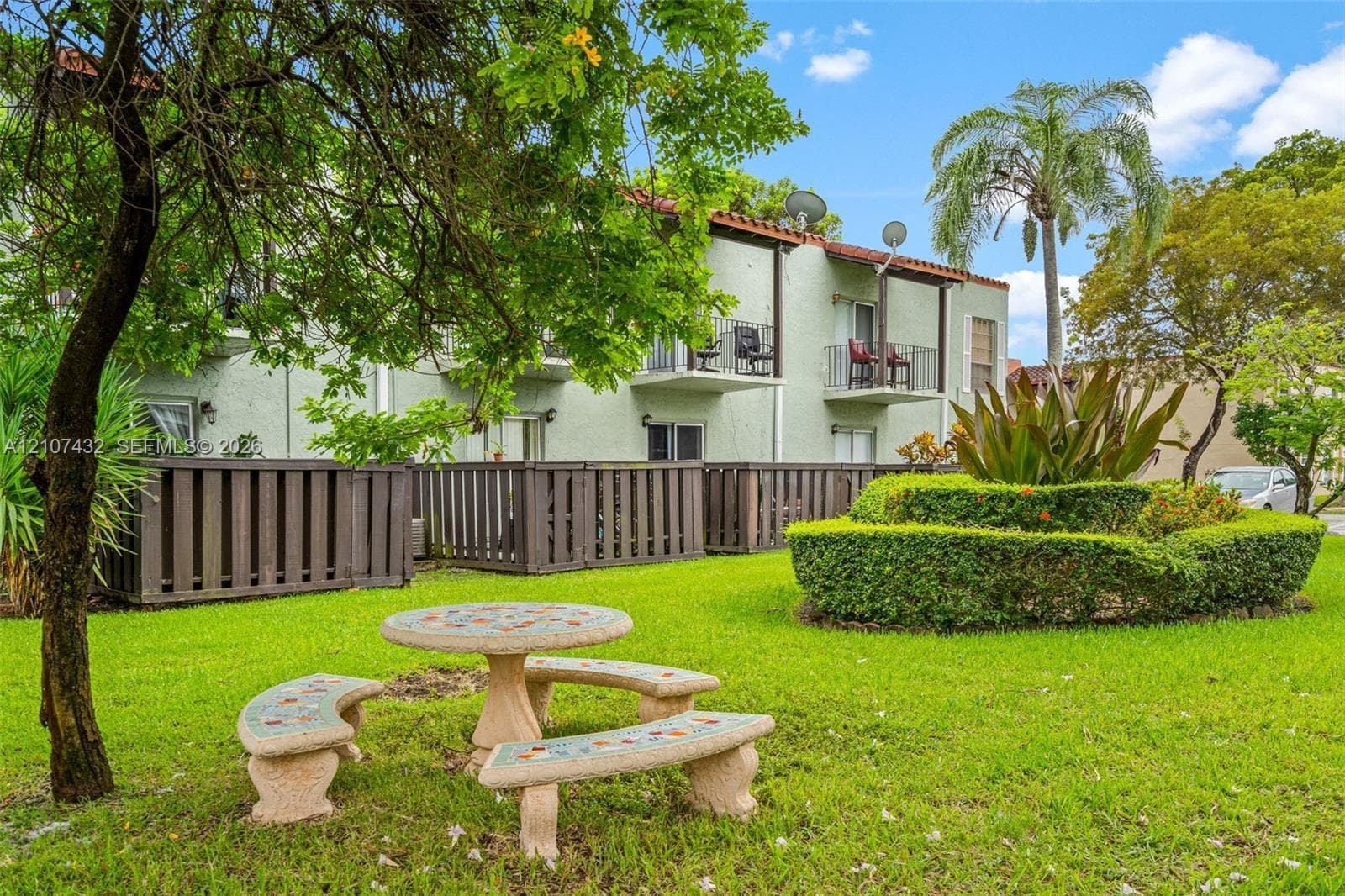 Stucco exterior featuring second-story balconies, manicured lawn, sculpted hedge, and mature landscaping
