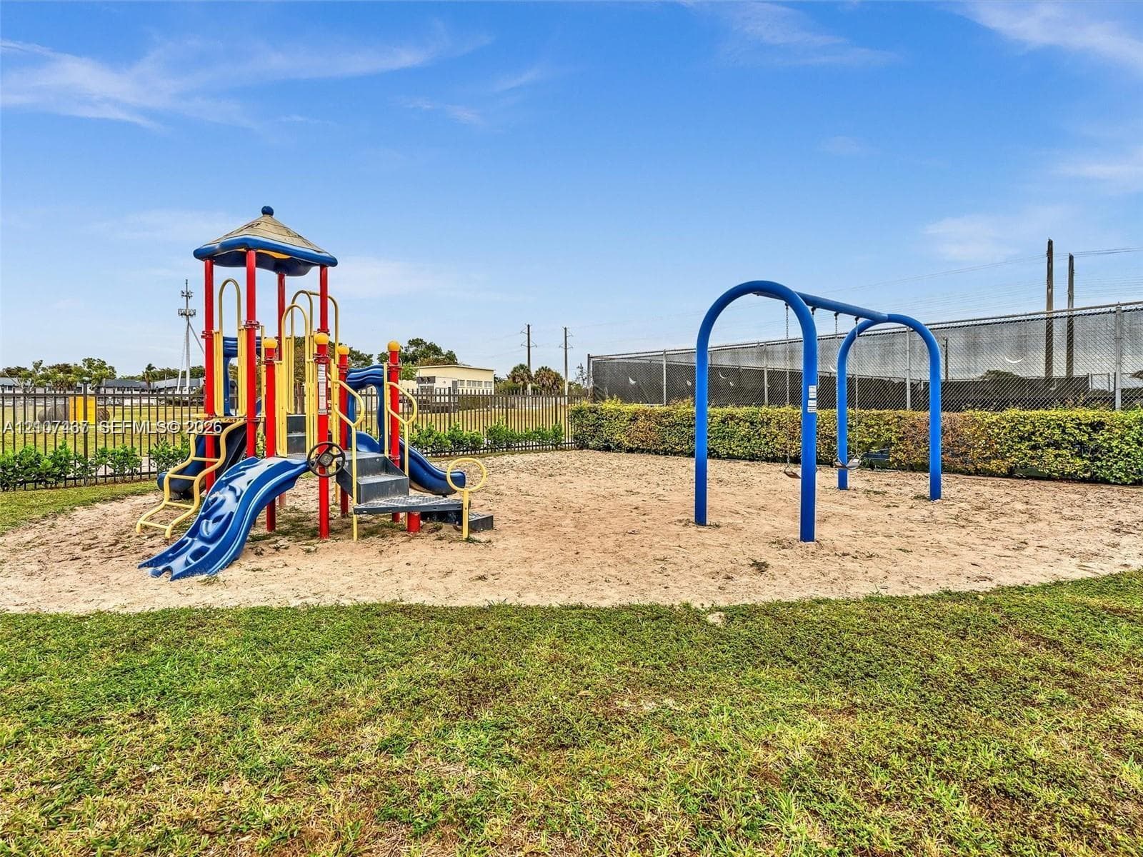 Recreational area featuring a structured playground set, swing set, sand surface, and perimeter fencing