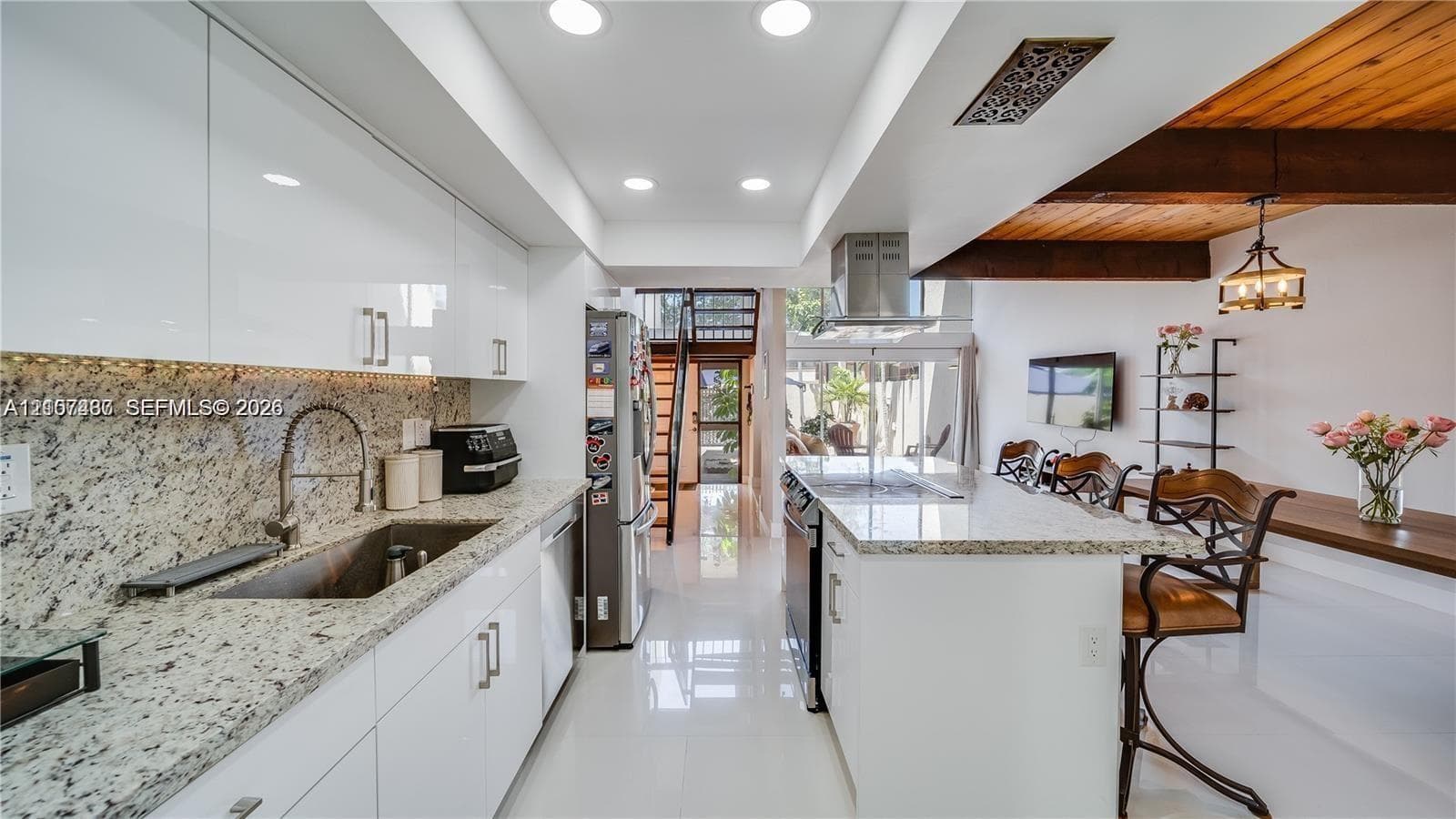 Contemporary kitchen featuring glossy flat-panel cabinetry, stone countertops, a large kitchen island, recessed lighting, and exposed ceiling beams