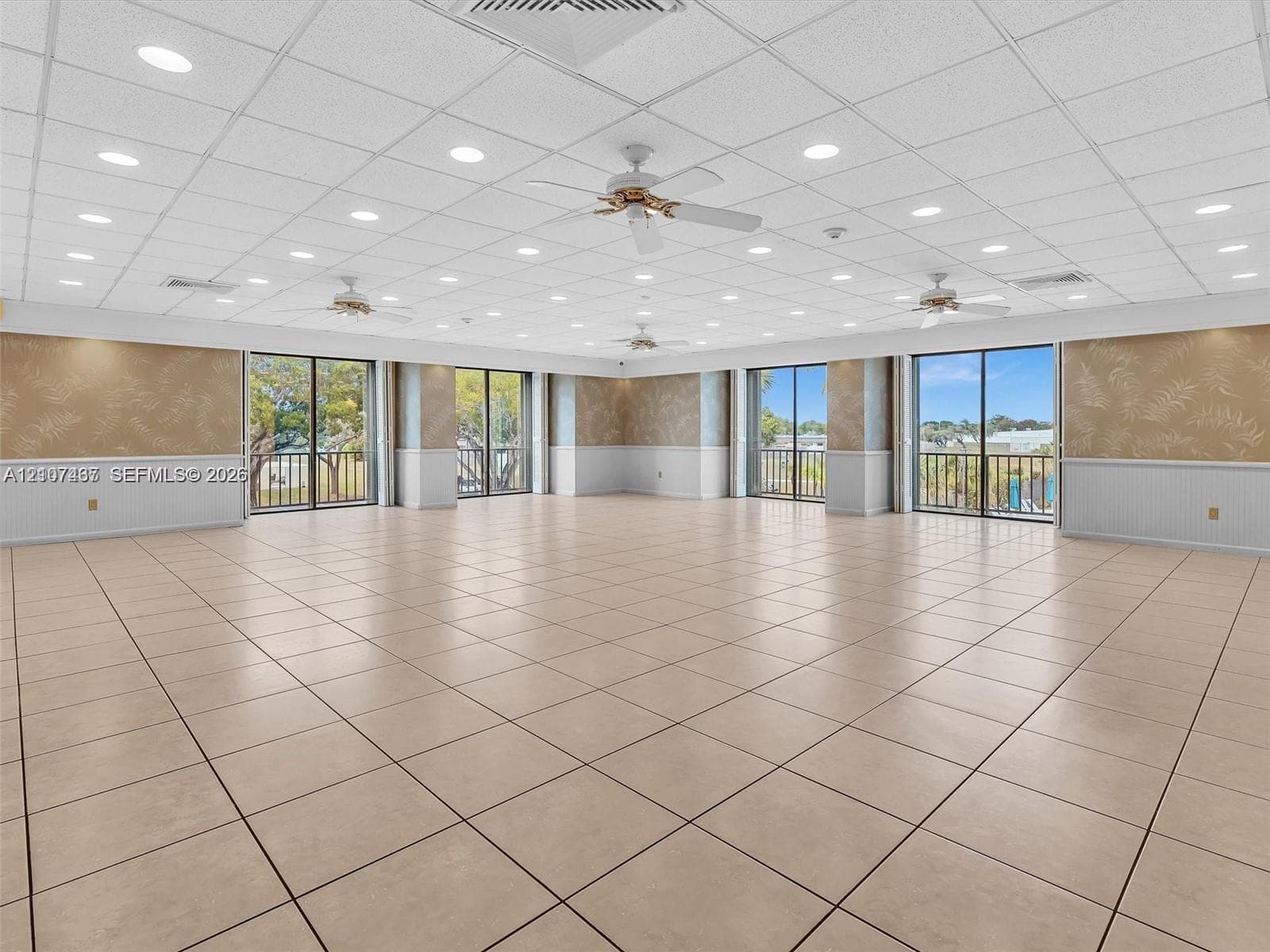 Expansive room featuring large-format tile flooring, multiple ceiling fans, recessed lighting, drop ceiling, and multiple glass sliding doors