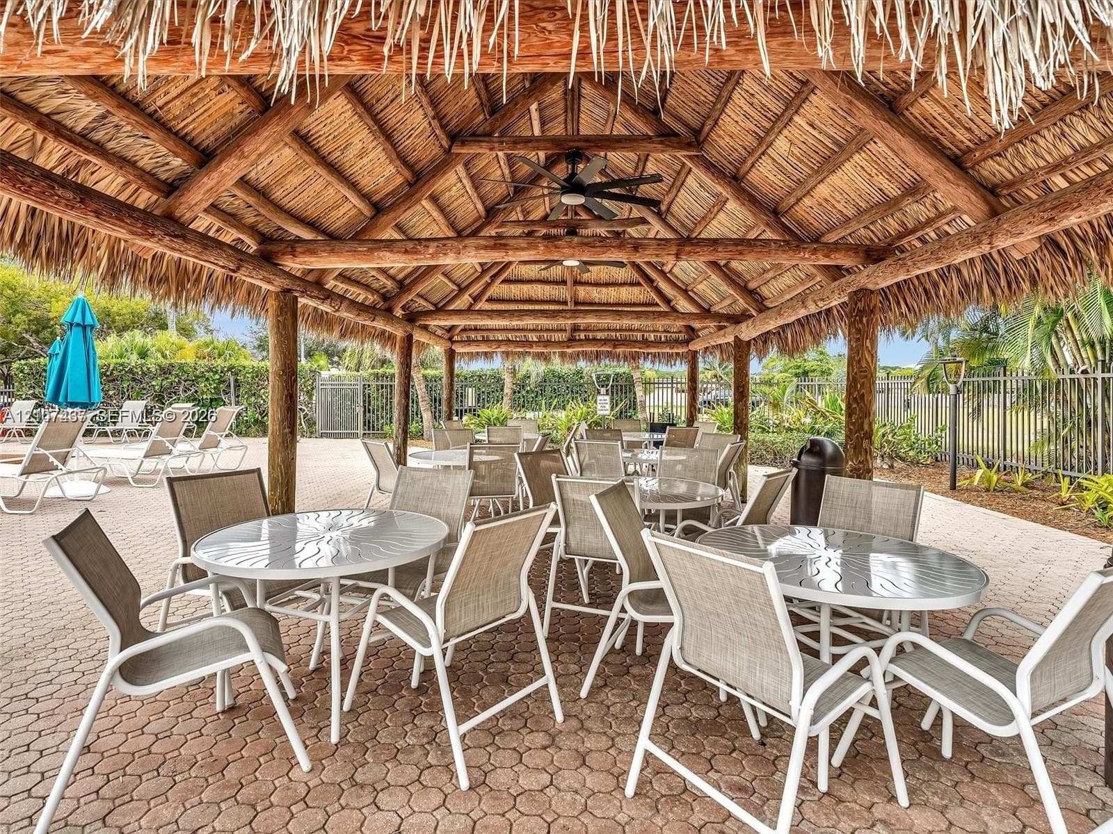 Covered outdoor pavilion featuring a rustic thatched roof, exposed timber beam construction, integrated ceiling fans, and concrete paver flooring