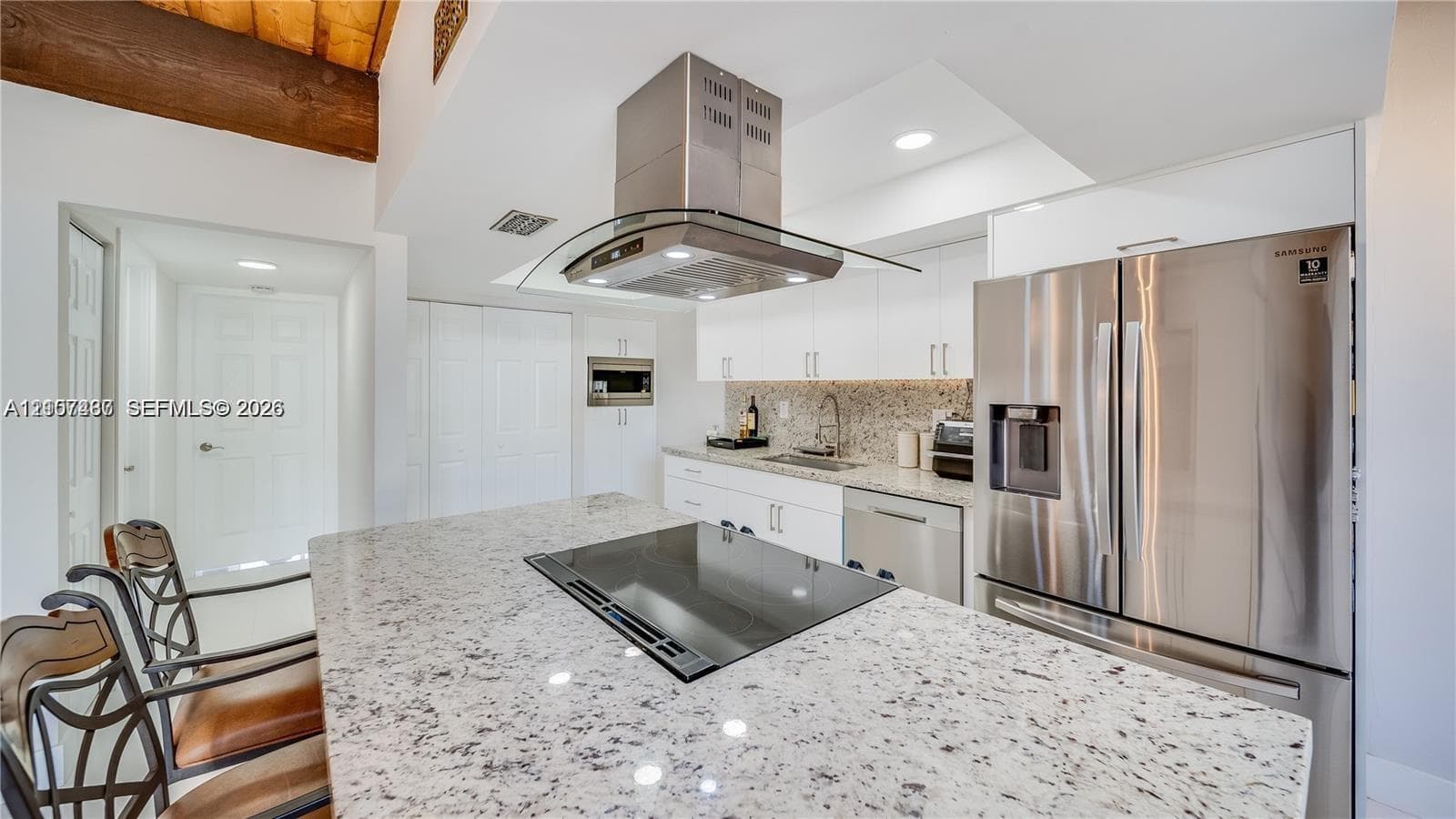 Kitchen featuring a center island with a cooktop, stone-finish countertops, stainless steel appliances, a glass range hood, and white cabinetry
