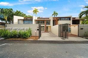 Modern stucco exterior featuring clean architectural lines, a gated paved driveway, and custom metal privacy fencing