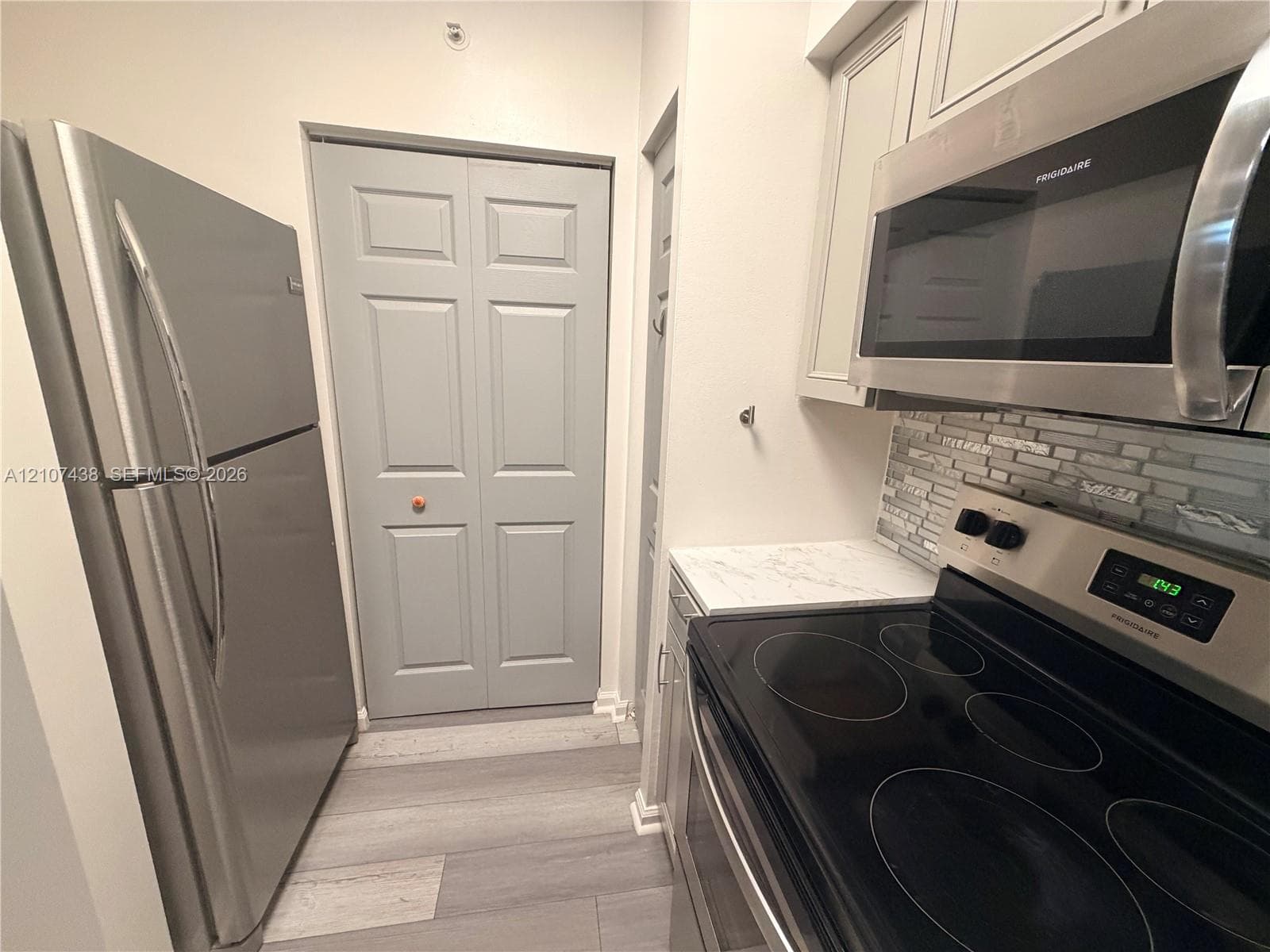 Stainless steel refrigerator, built-in microwave, flat-top electric range, stone-composite backsplash, and wood-finish flooring