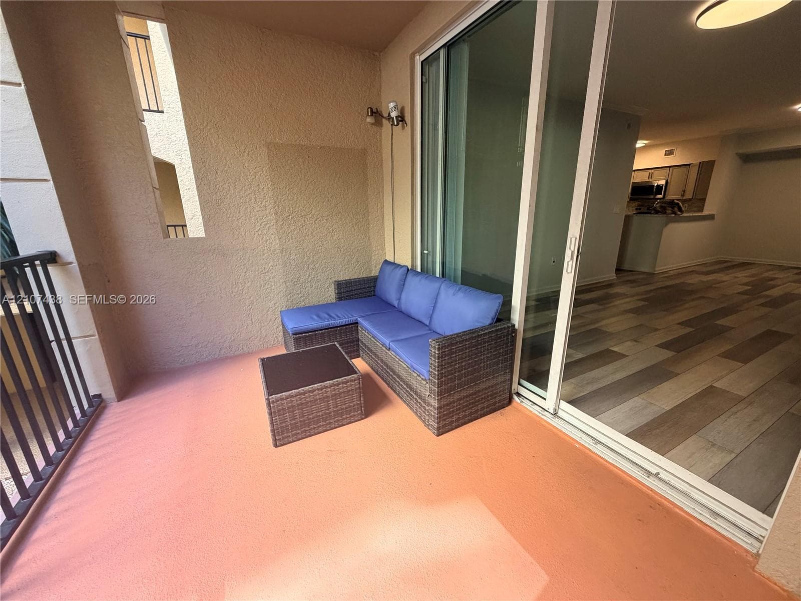 Covered balcony featuring a metal railing, wall-mounted exterior lighting, and sliding glass door entry to interior wood-finish flooring