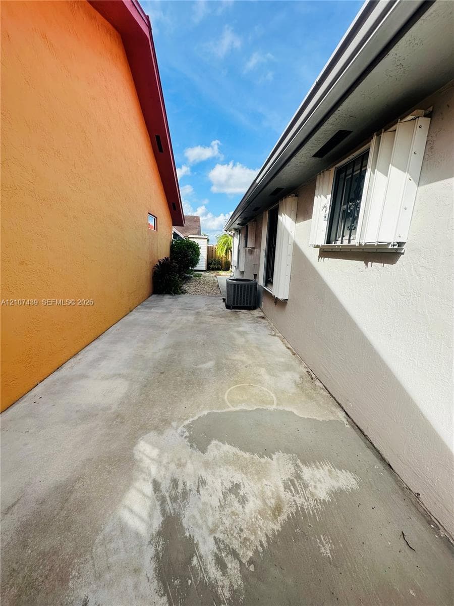 Concrete side yard featuring stucco exterior walls, installed storm shutters, and an external HVAC unit