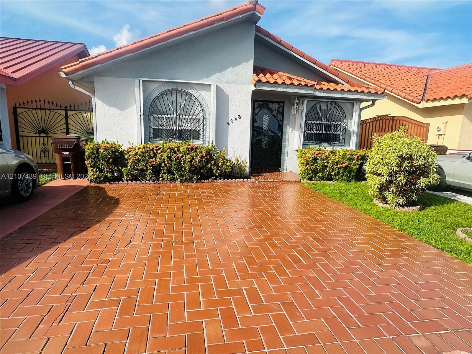 Stucco exterior featuring a red clay tile roof, herringbone-patterned brick paver driveway, and arched window detailing