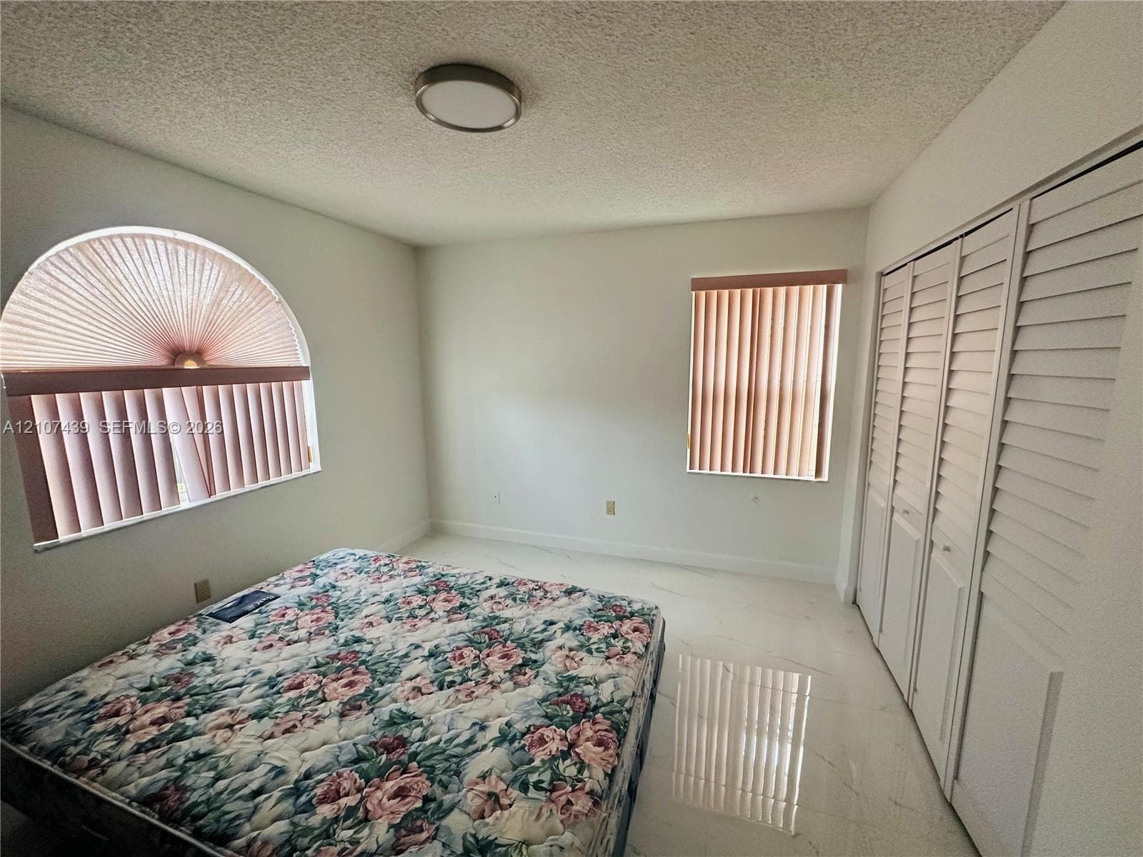 Arch-top window, rectangular window with vertical blinds, tile flooring, and floor-to-ceiling closet with louvered doors