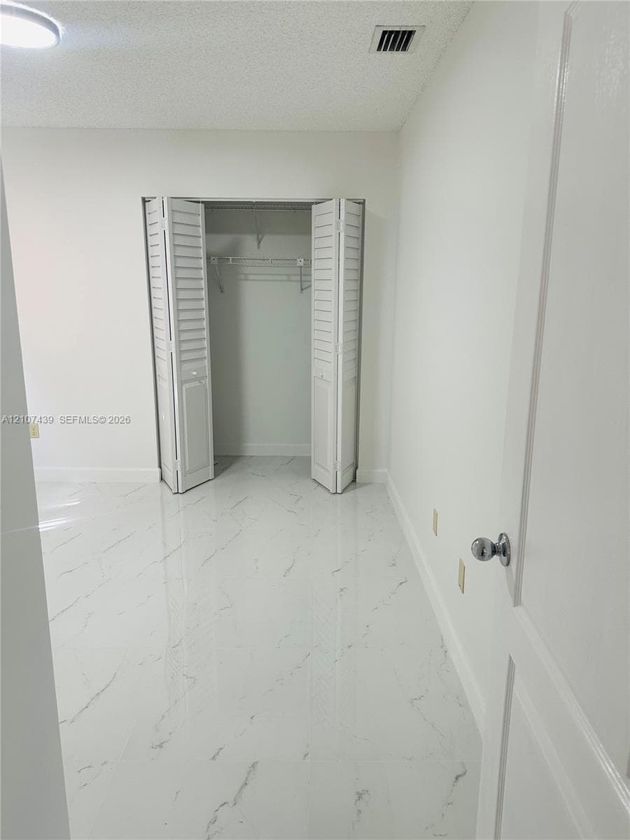 White tile flooring with grey veining, closet with bi-fold louvered doors, and a round ceiling-mounted light fixture