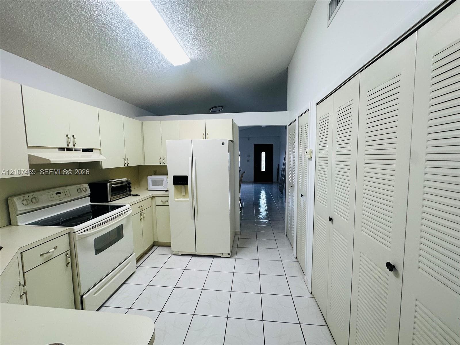 Kitchen featuring cabinetry, white tile flooring, built-in side-by-side refrigerator, white range, and louvered closet doors