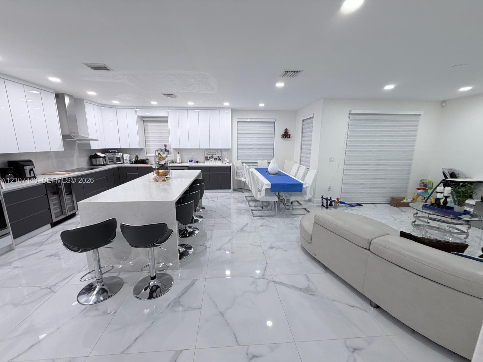 Kitchen featuring two-tone flat-panel cabinetry, a central island with stone-finish countertops, large-format tile flooring, stainless steel range hood, and recessed lighting