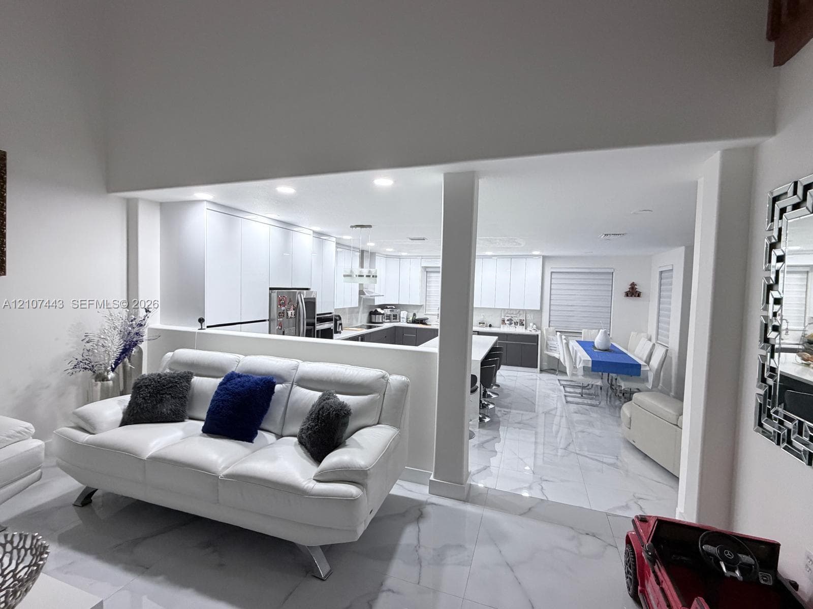 Open-concept interior featuring large-format polished tile flooring, white cabinetry with integrated hardware, recessed lighting, and a breakfast bar