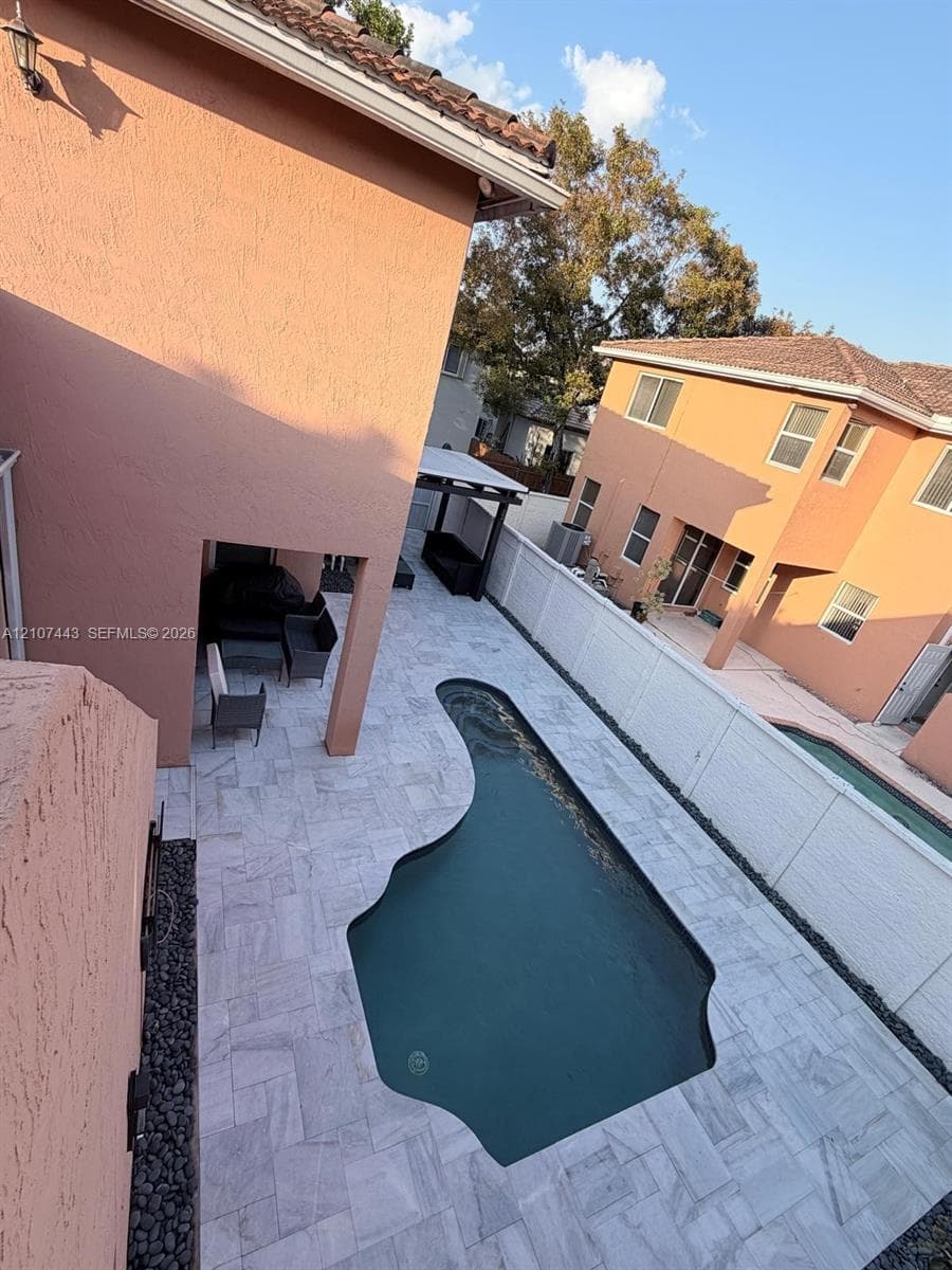 Stucco exterior residence featuring an in-ground pool, stone-paver patio, covered porch, and white vinyl privacy fencing