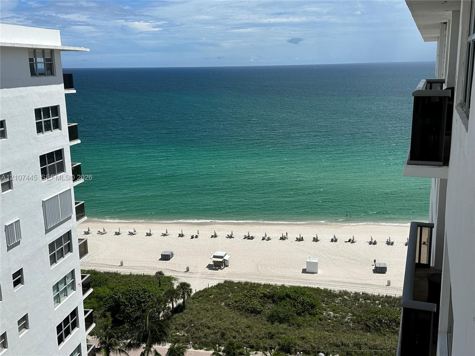 Elevated oceanfront perspective featuring a private balcony, sandy beach access, and panoramic coastal horizon