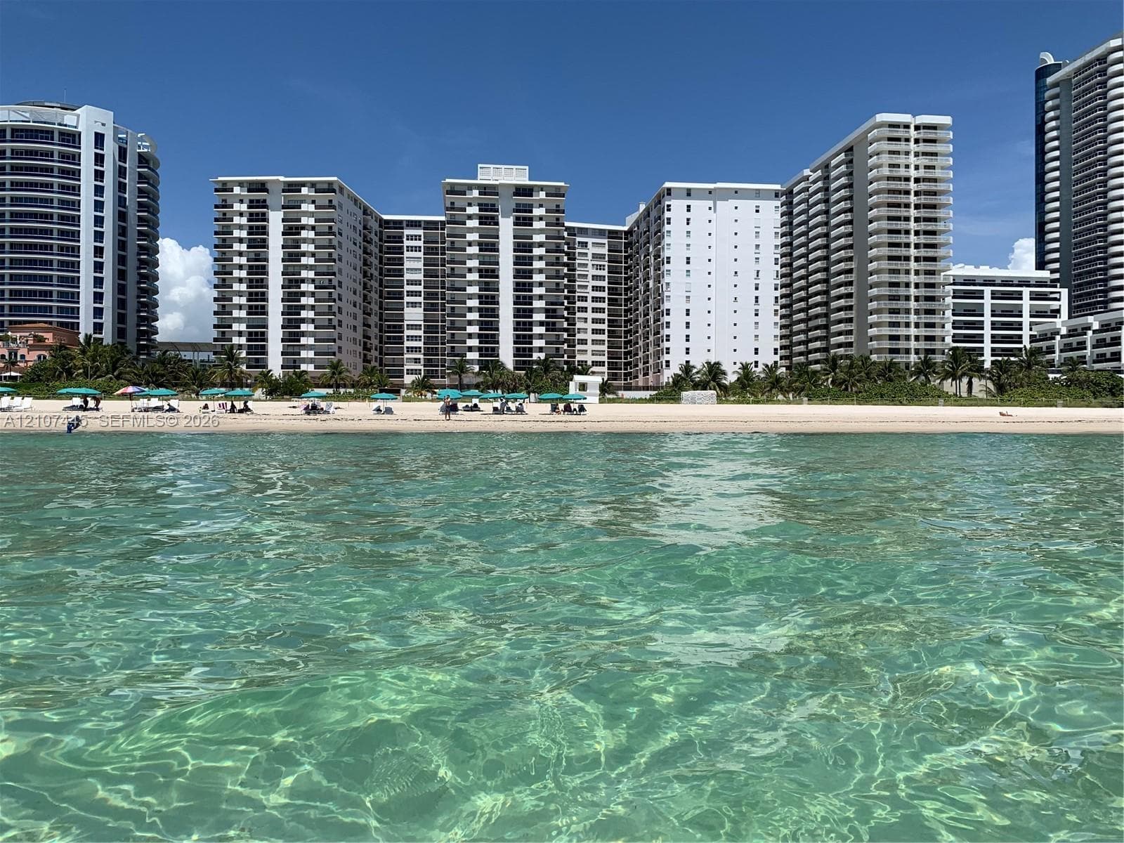 Direct oceanfront property featuring sandy shoreline, turquoise waters, and multi-story high-rise architecture