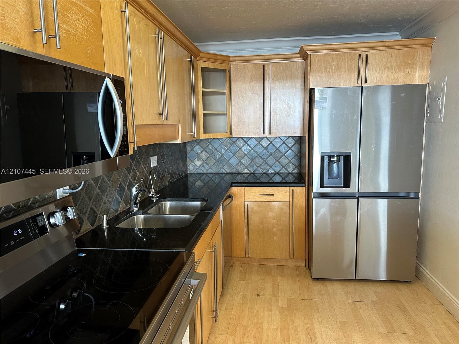 Kitchen featuring natural finish cabinetry, dark stone countertops, stainless steel appliances, diamond-pattern tile backsplash, and light-tone wood-finish flooring