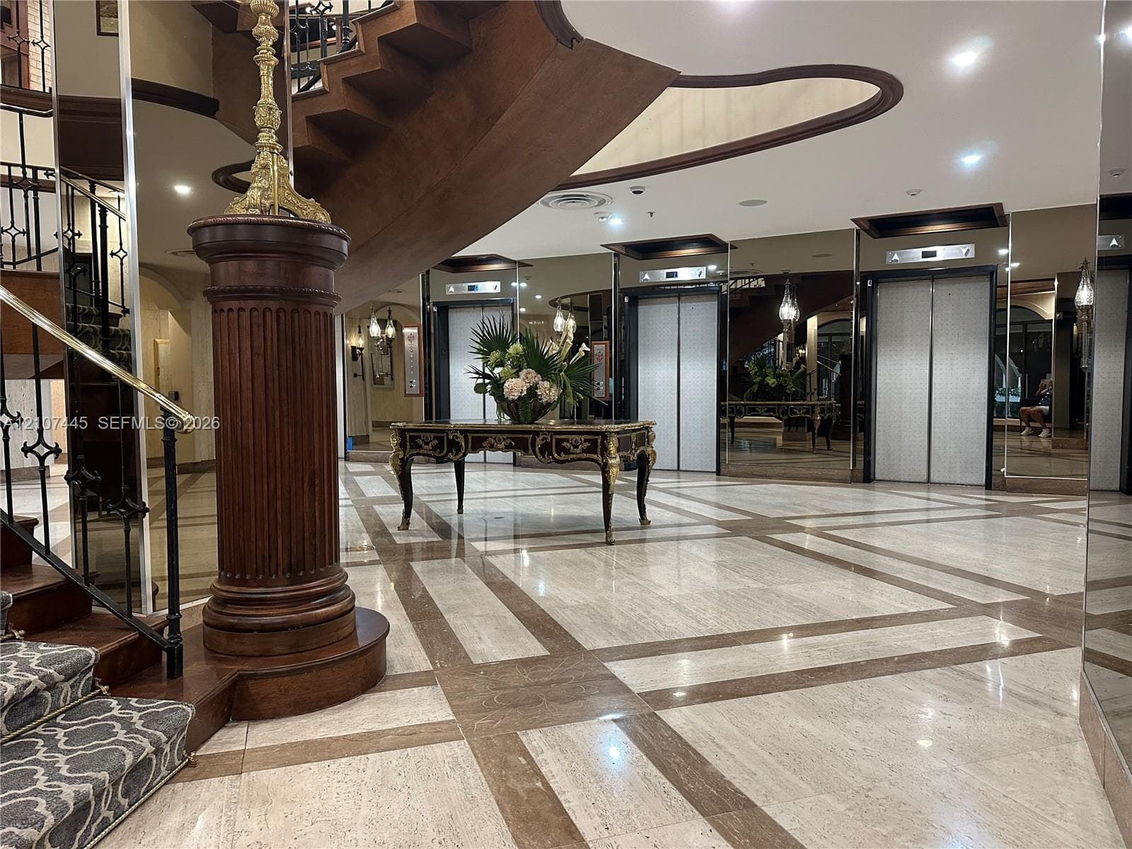 Grand foyer featuring polished stone flooring with geometric inlays, a curved wooden staircase with ornate detailing, and integrated elevator access