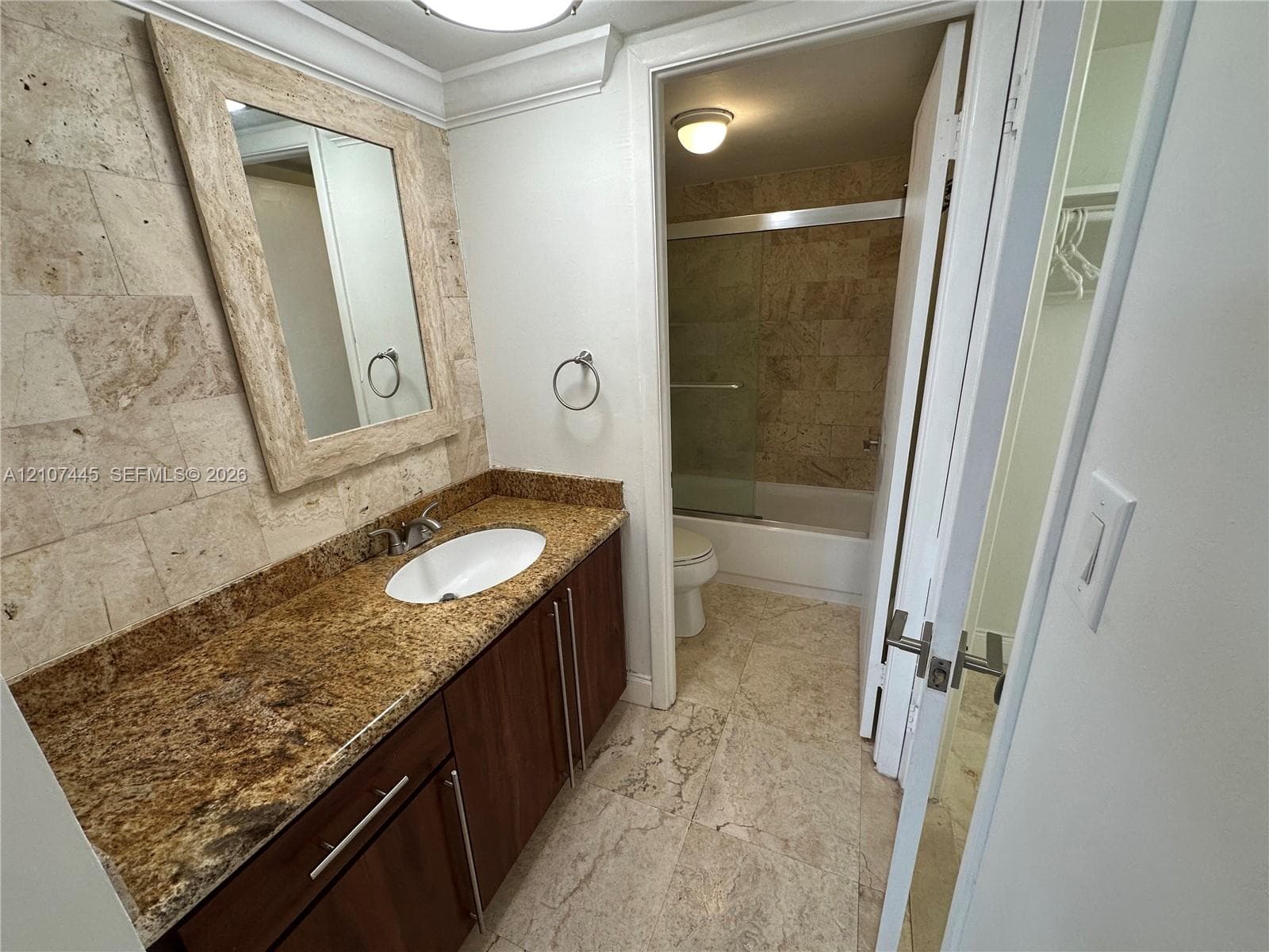 Bathroom featuring a vanity with wood-finish cabinetry, stone countertop with an undermount sink, matching stone-tiled walls, and a separate tub and shower enclosure with a glass door