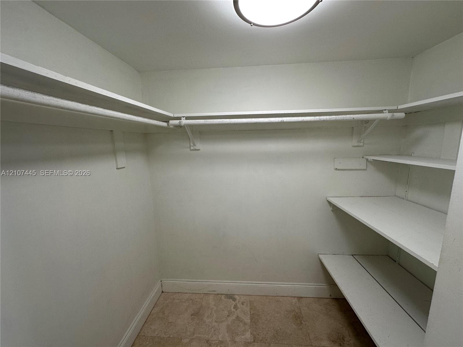 Walk-in storage space featuring built-in shelving, integrated hanging rods, and stone-finish flooring