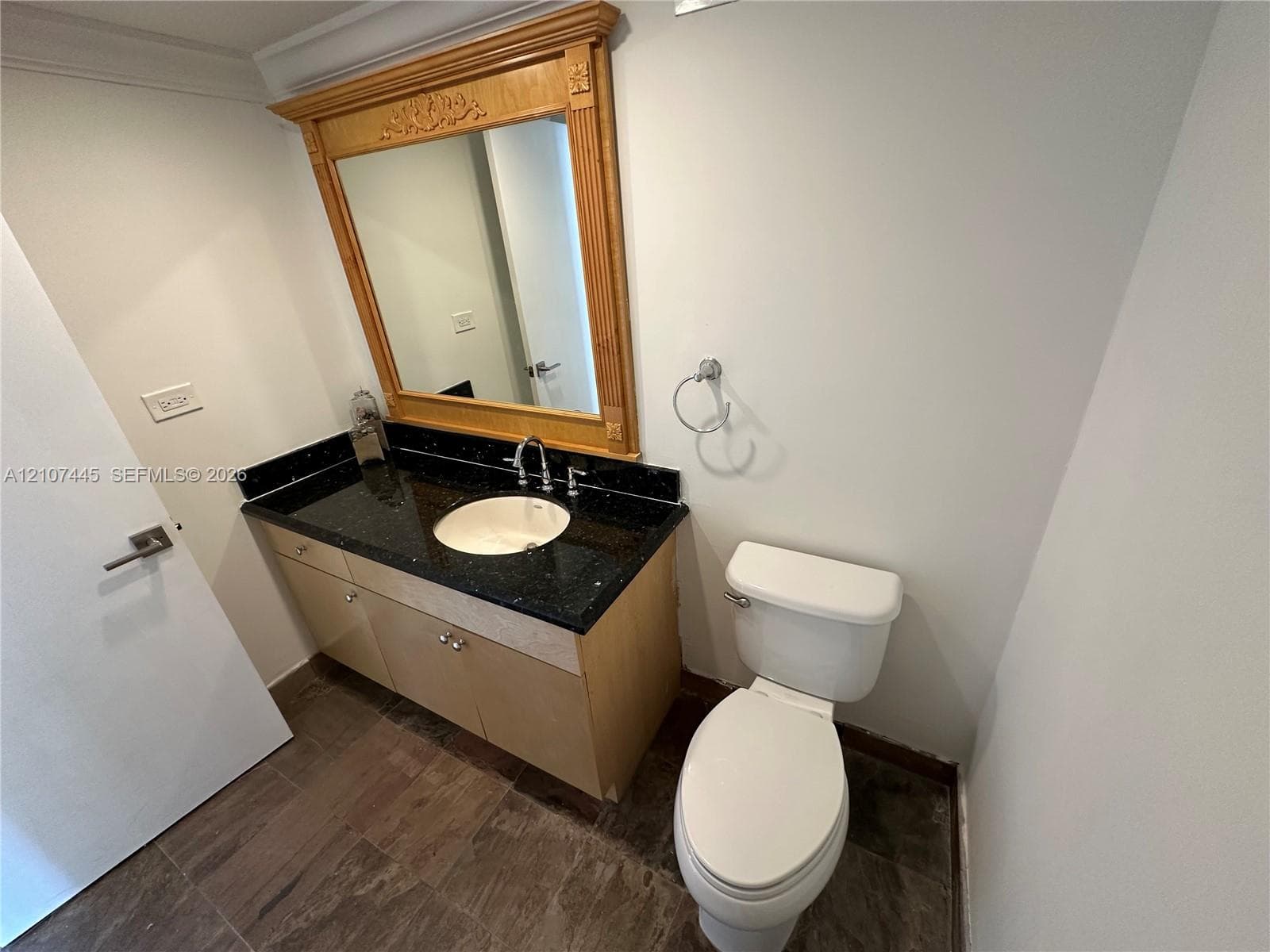 Vanity featuring a dark stone countertop, integrated basin, light wood cabinetry, and a decorative wood-framed mirror, complemented by wood-finish flooring