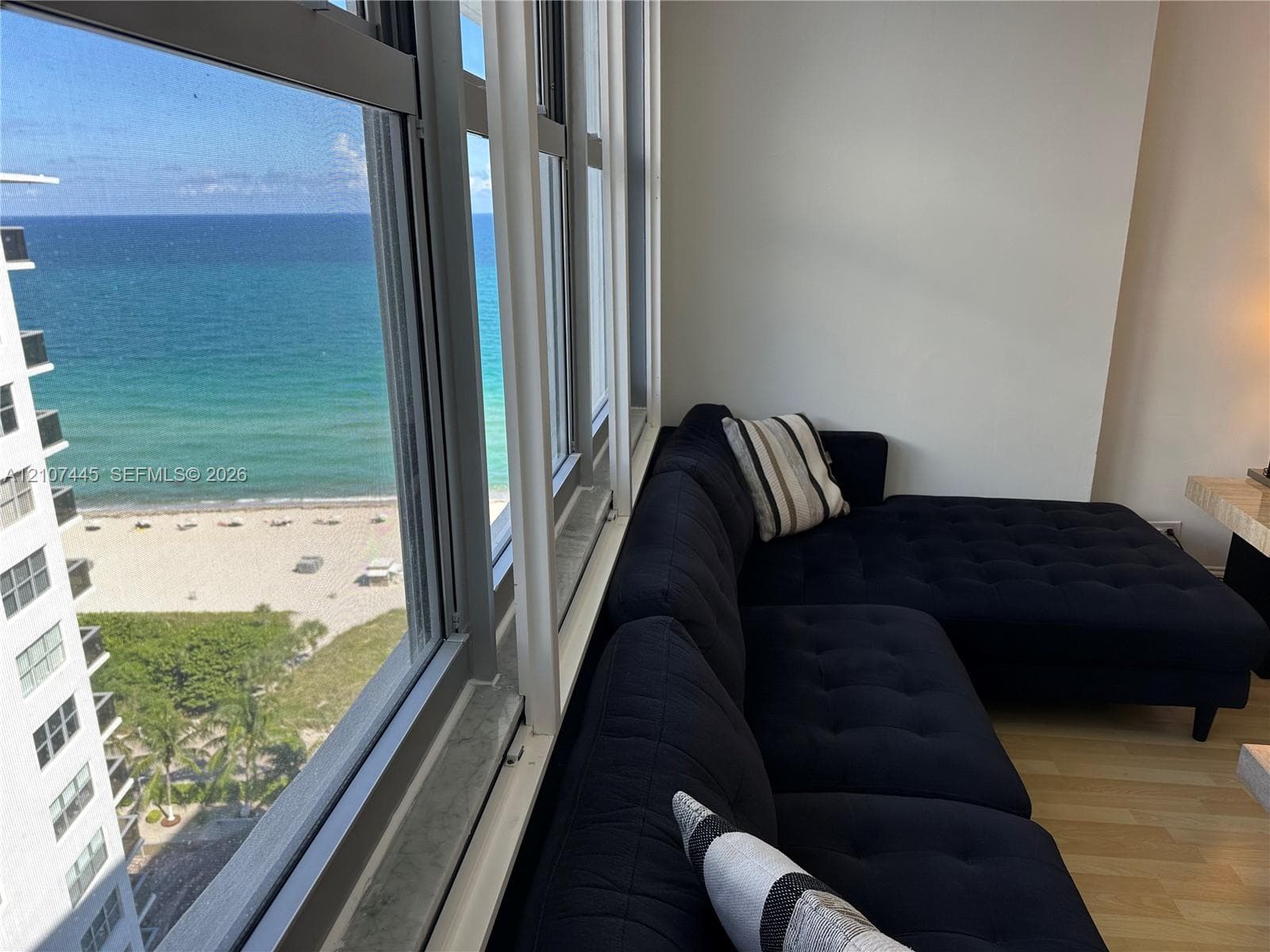 Floor-to-ceiling windows featuring ocean and beach scenery, wood-finish flooring, and white interior walls
