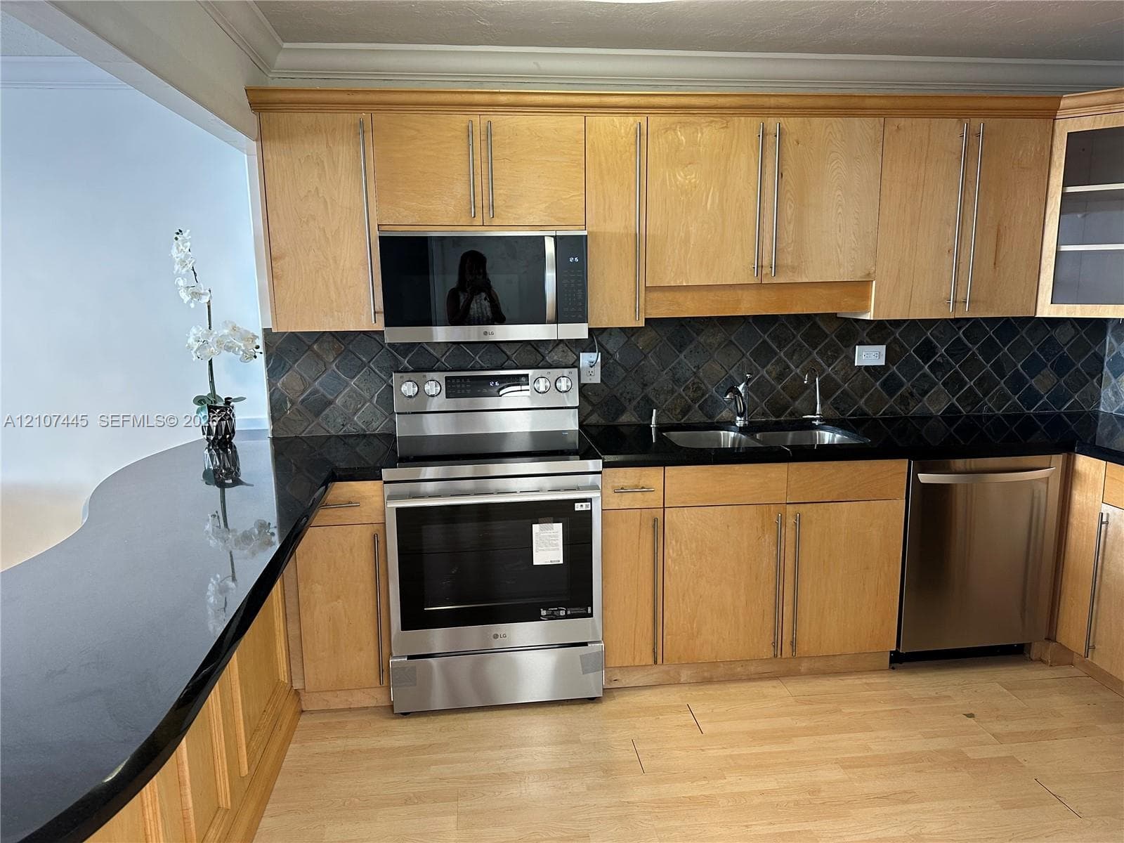 Kitchen featuring natural wood cabinetry, polished black stone countertops, stainless steel appliances, and a tiled backsplash