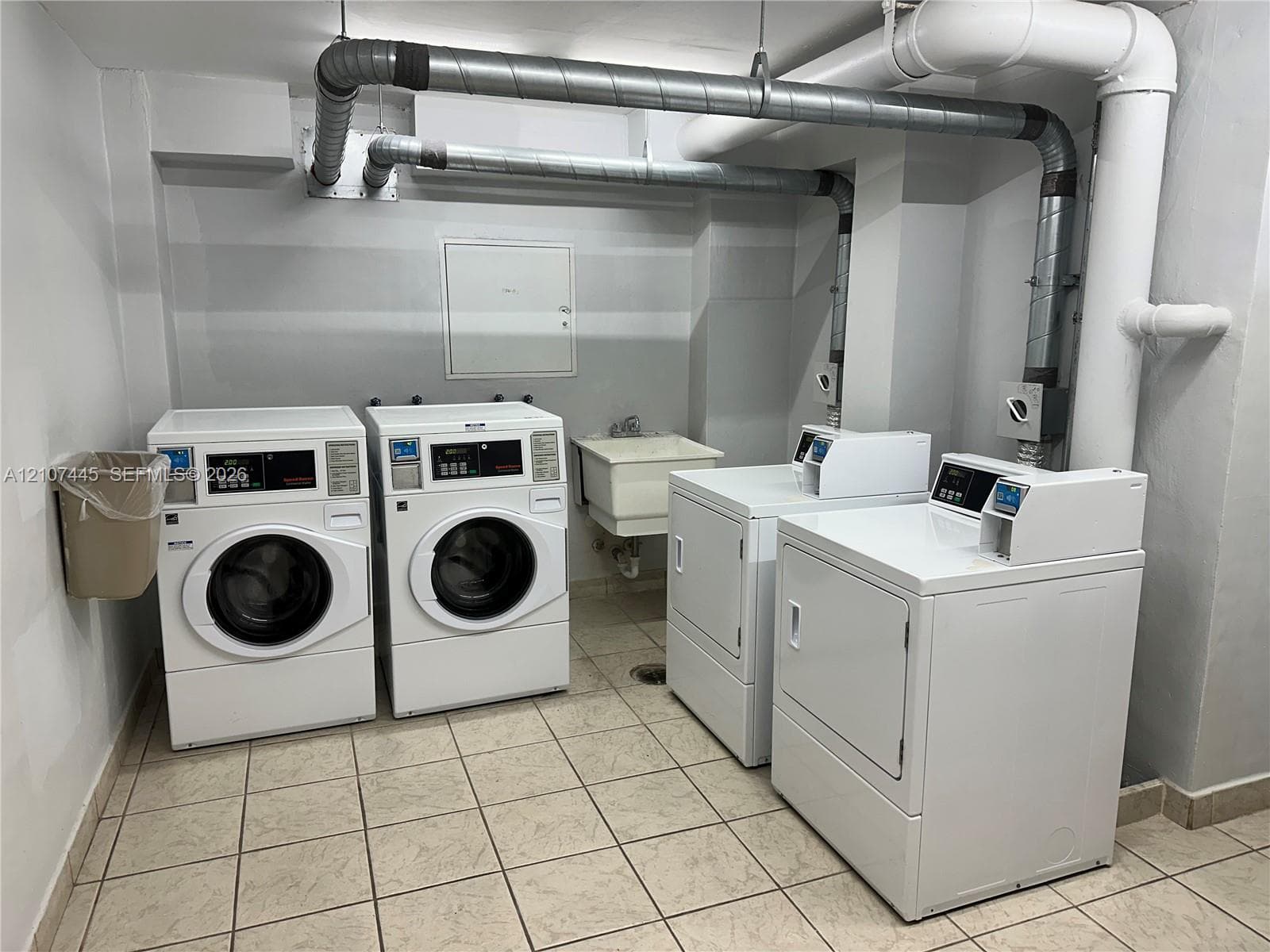 Laundry room featuring two front-loading washers, two dryers, a utility sink, and tile flooring
