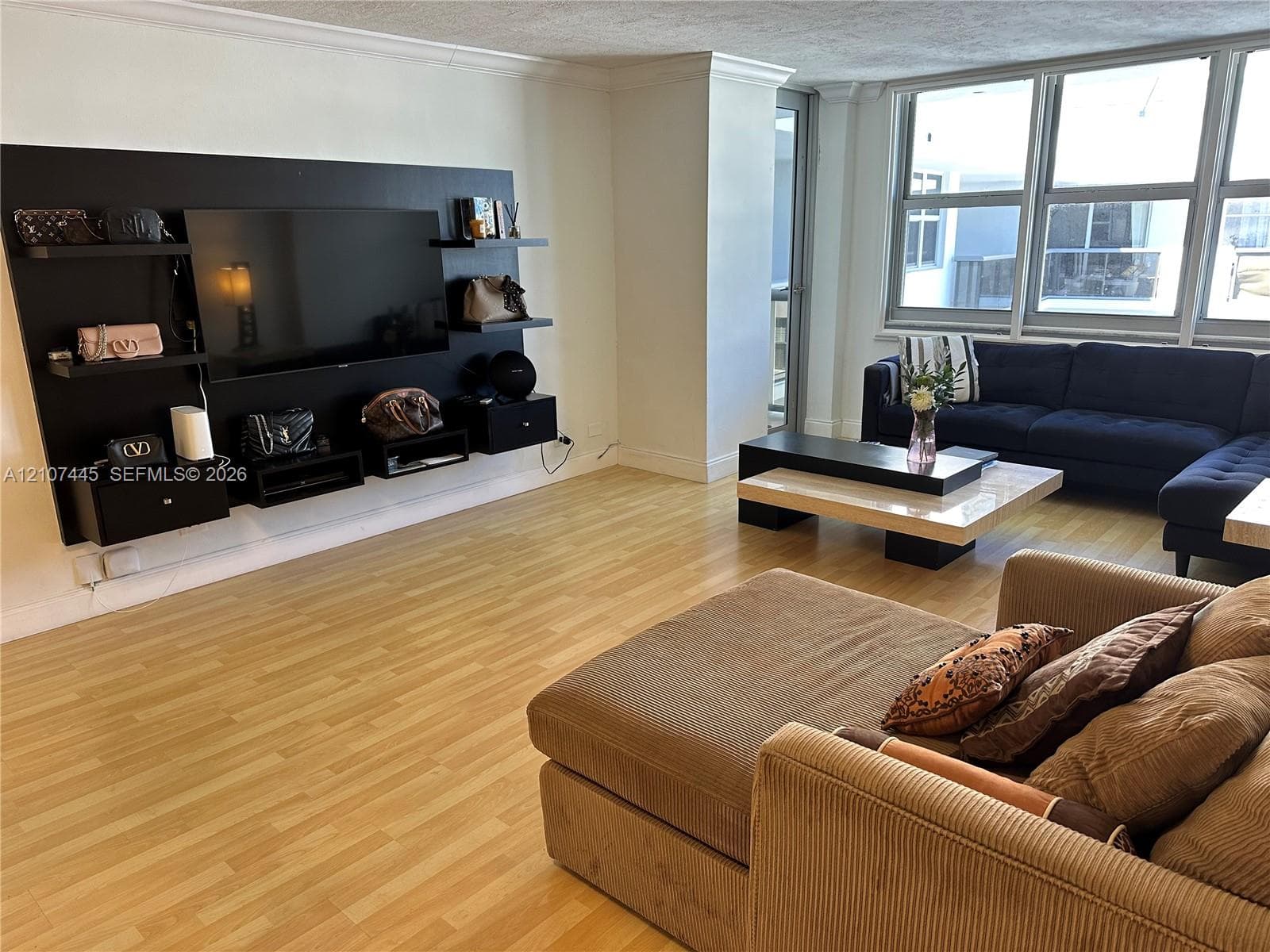 Living space featuring light wood-finish flooring, custom black wall-mounted shelving unit, and large floor-to-ceiling windows