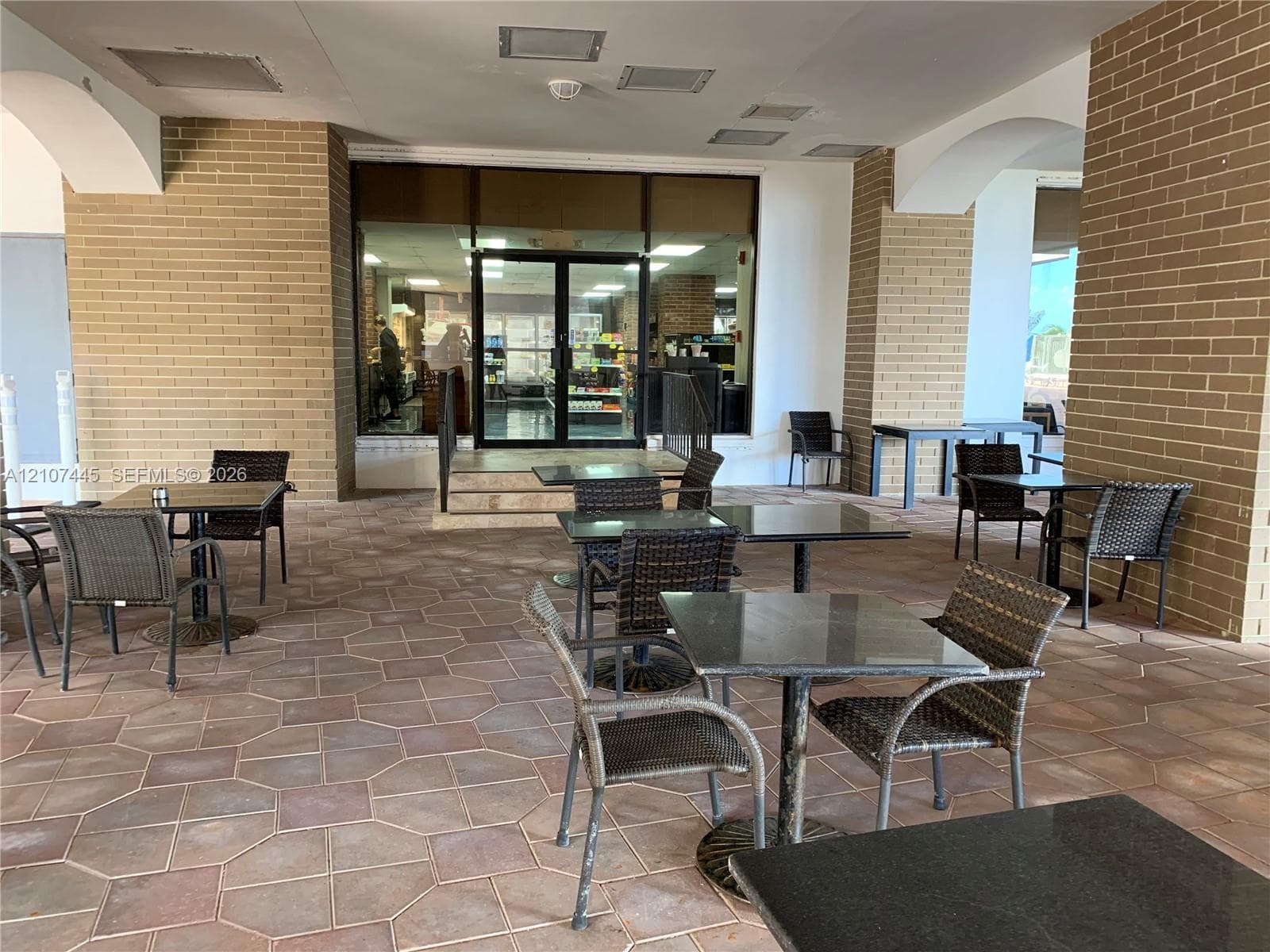 Covered exterior patio featuring brick masonry columns, arched architectural details, and stone-tile flooring