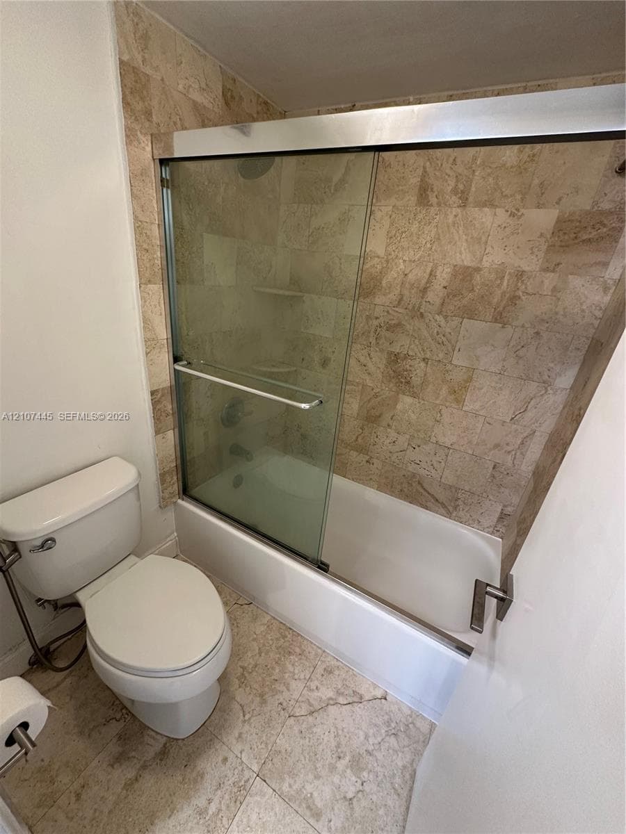 Tiled shower enclosure featuring natural stone wall tile, sliding glass shower doors, built-in shelving, and stone floor tiling