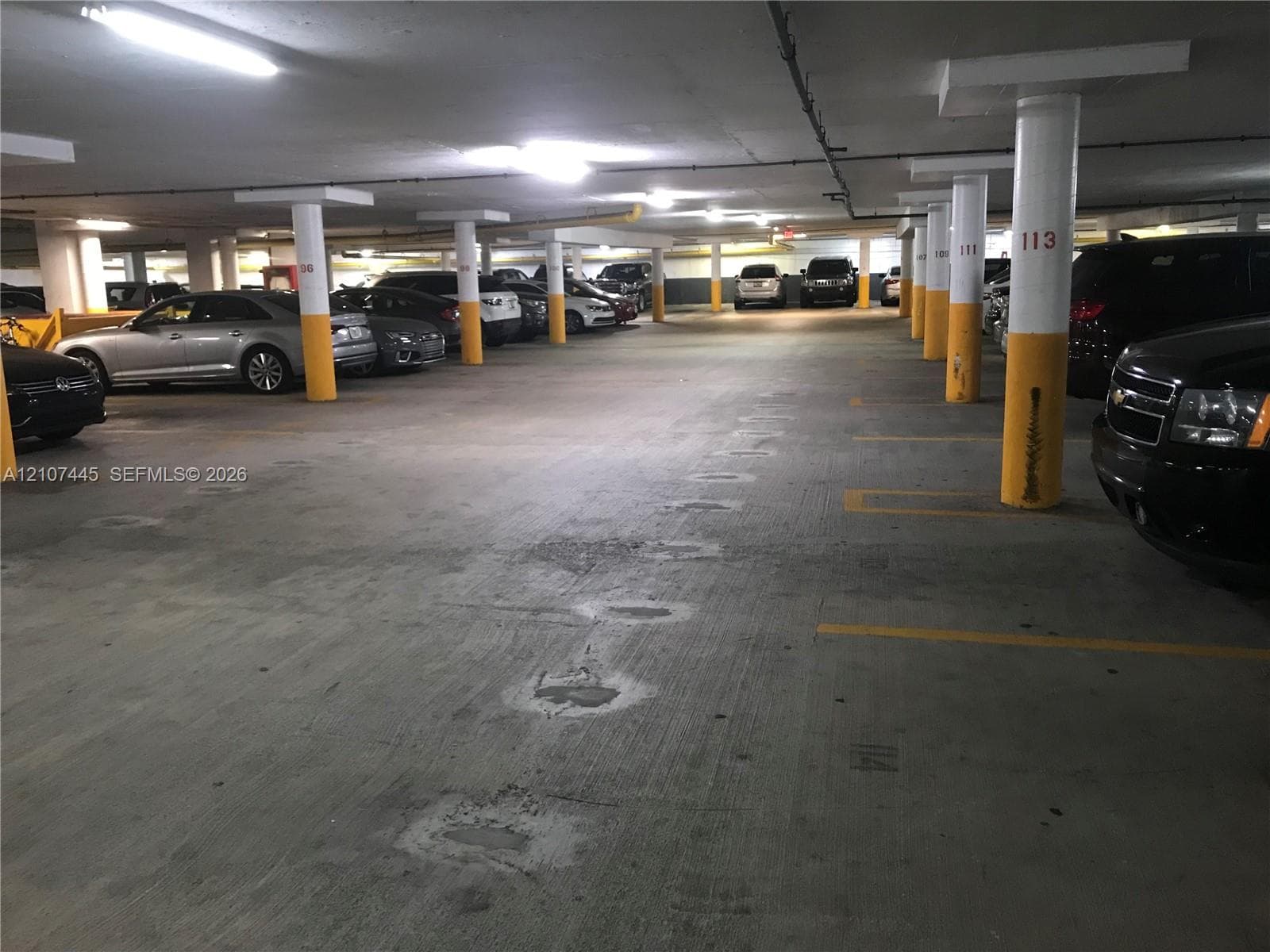 Covered parking garage featuring concrete flooring, structural support columns, and overhead lighting