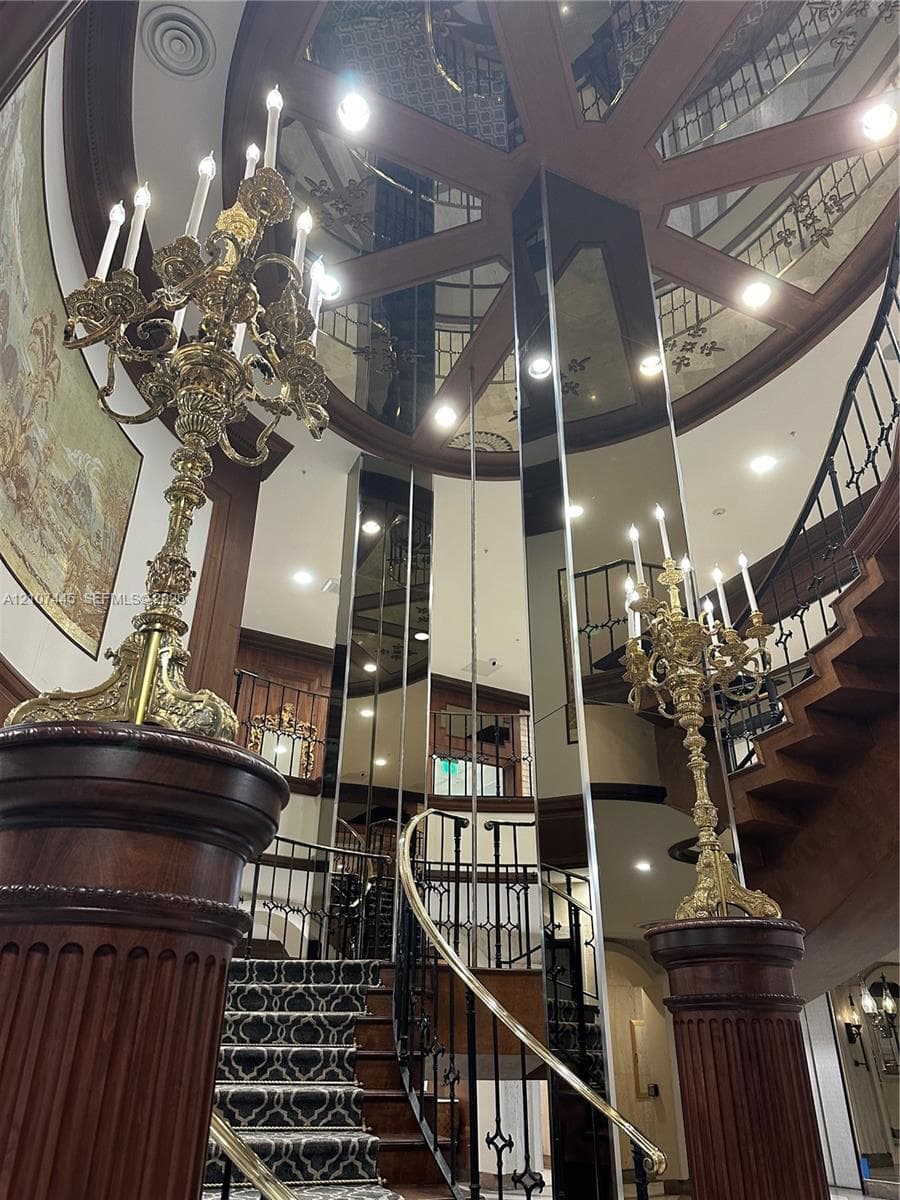 Grand foyer featuring a custom curved staircase with intricate wrought-iron railings, wood-paneled columns, full-height mirrored wall accents, and a circular recessed ceiling
