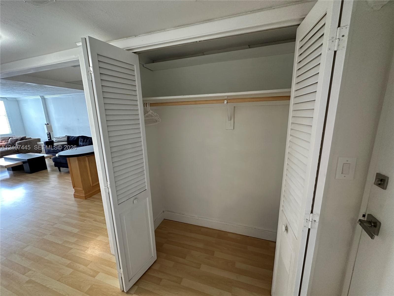 Closet featuring white louvered bifold doors, an integrated upper storage shelf, and a wooden hanging rod