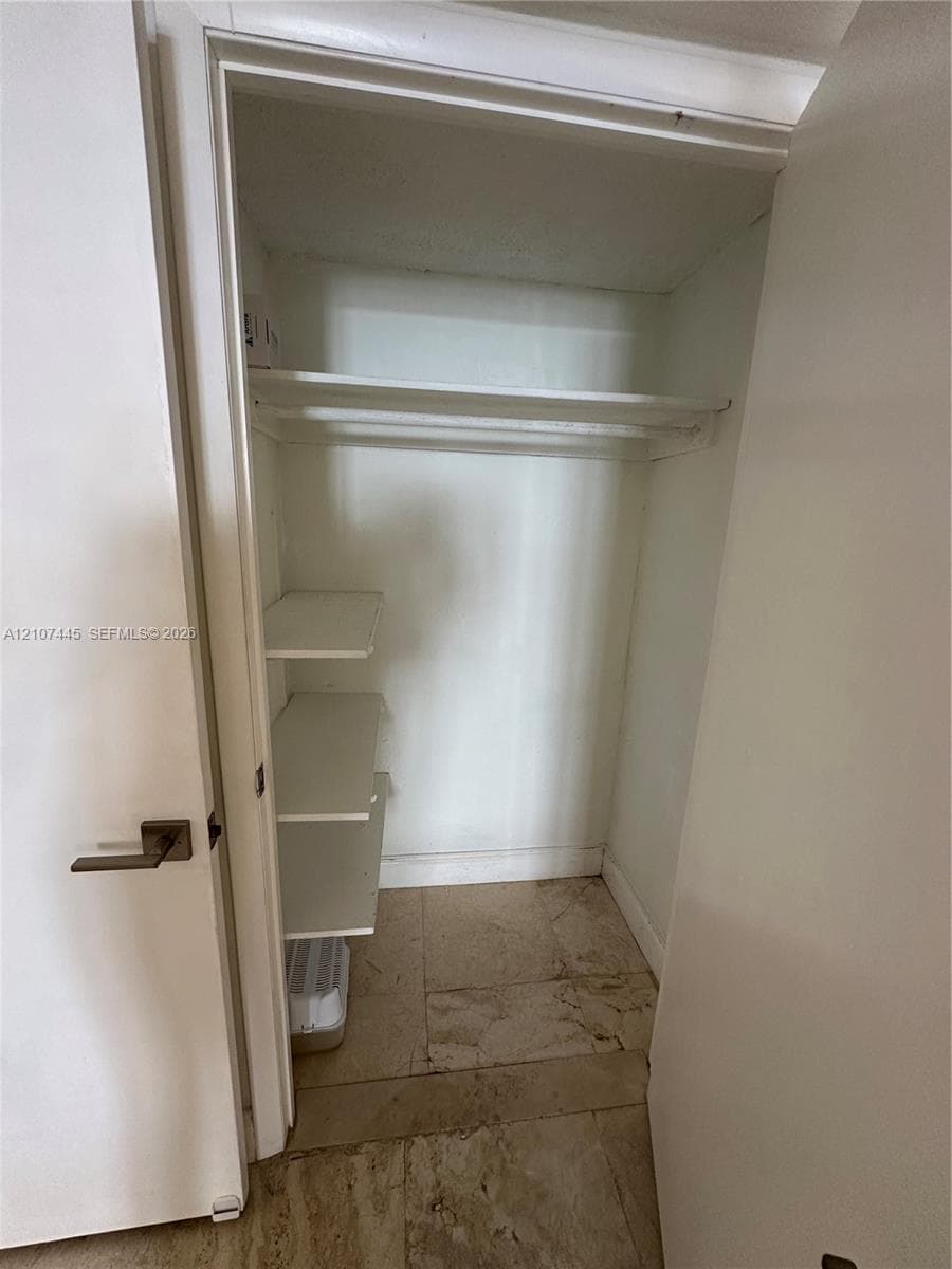 Storage closet featuring built-in shelving, a dedicated overhead shelf, and stone-finish flooring