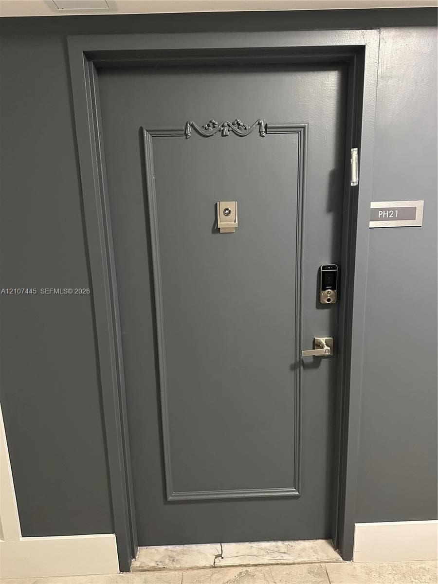 Gray-toned door featuring decorative millwork trim, a central peephole, and a metal electronic keypad entry system