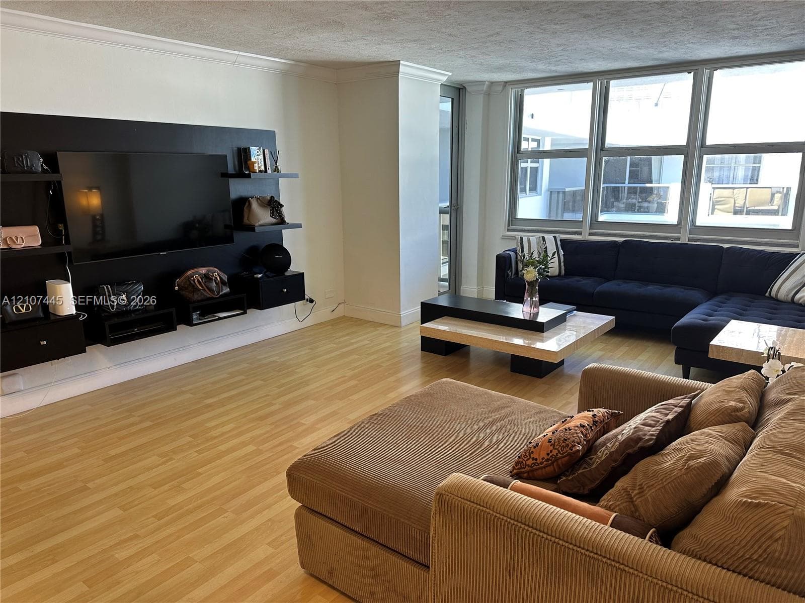 Living space featuring light-toned wood-finish flooring, floor-to-ceiling windows, and a built-in dark finish media console with tiered shelving