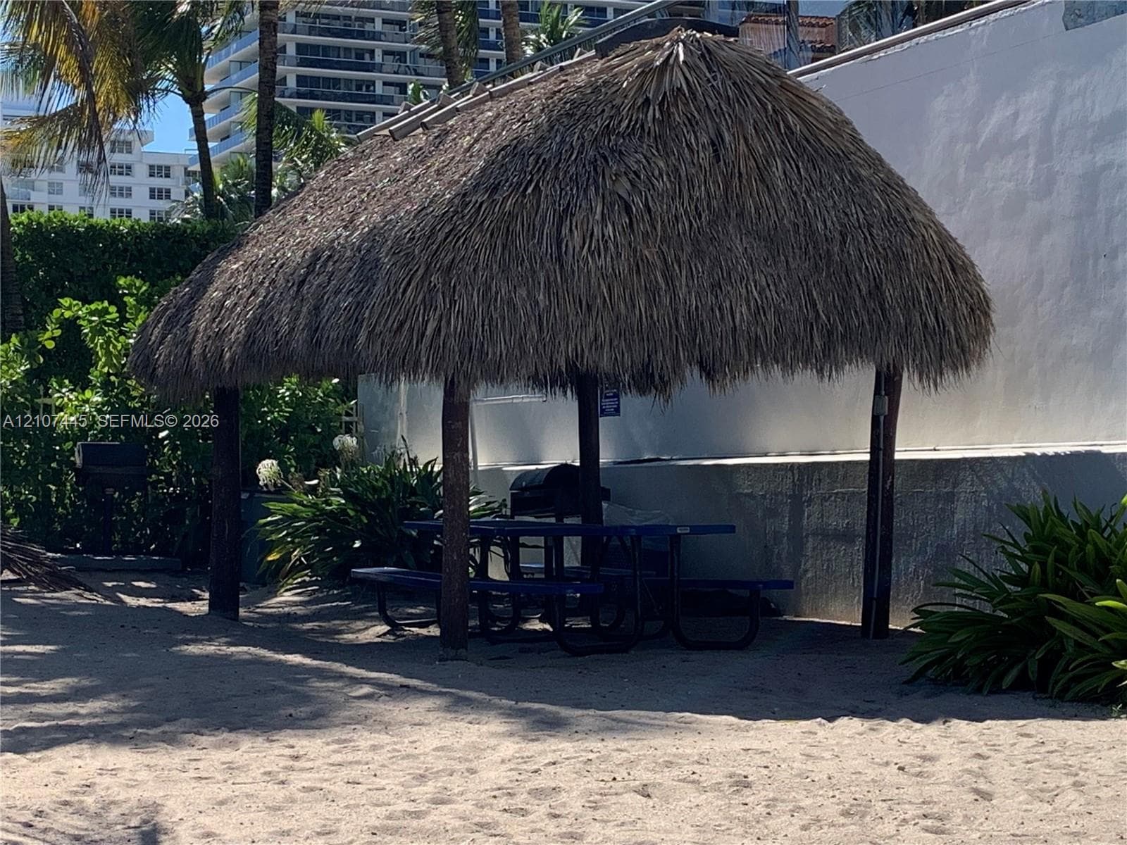 Thatch-roofed structure featuring timber support posts set on a sandy surface