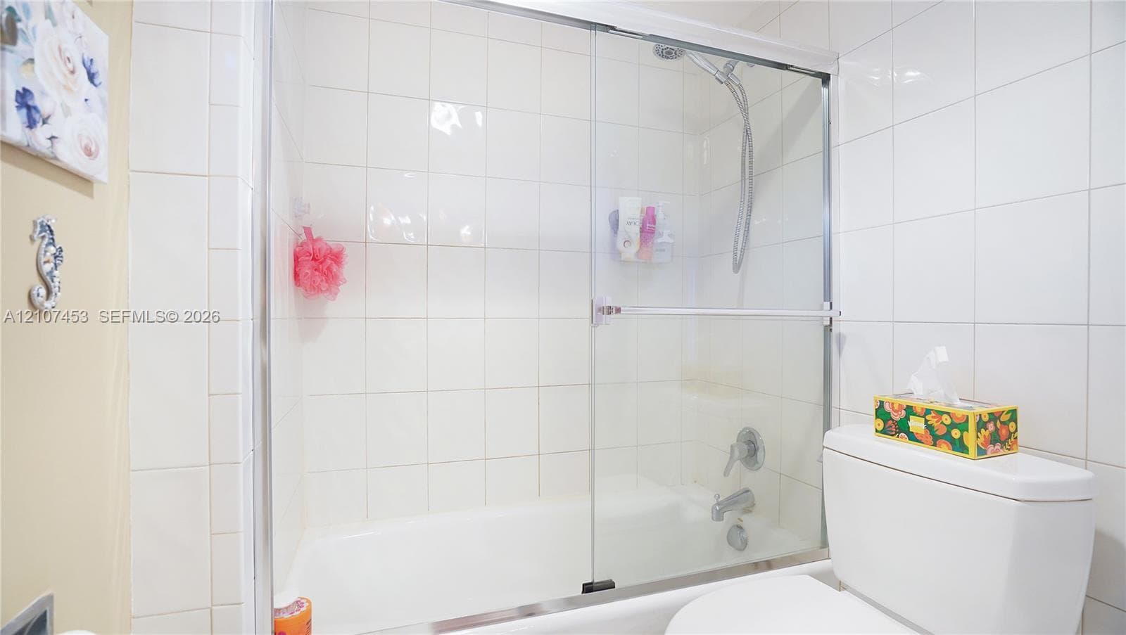 Bathtub and shower combination featuring full-height white wall tiling, sliding glass enclosure, chrome fixtures, and a handheld shower head
