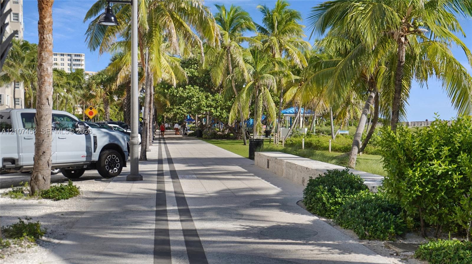 Paved promenade featuring stone-finish hardscaping, mature palm trees, integrated stone seating, and modern post lighting