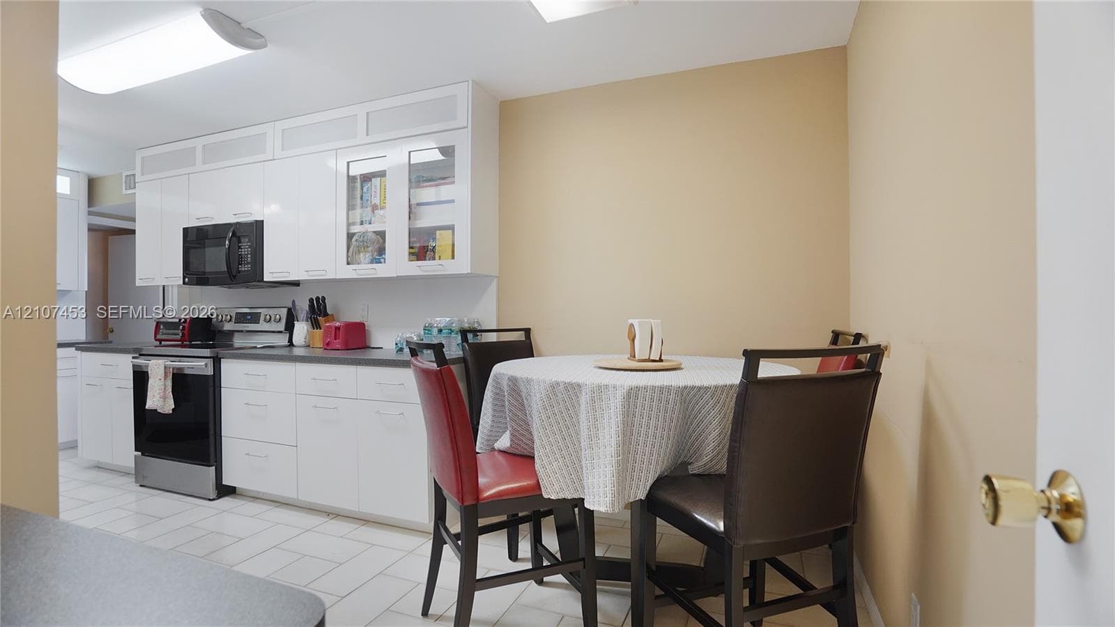 Kitchen featuring high-gloss white cabinetry, glass-paneled upper cabinets, stainless steel appliances, and ceramic tile flooring