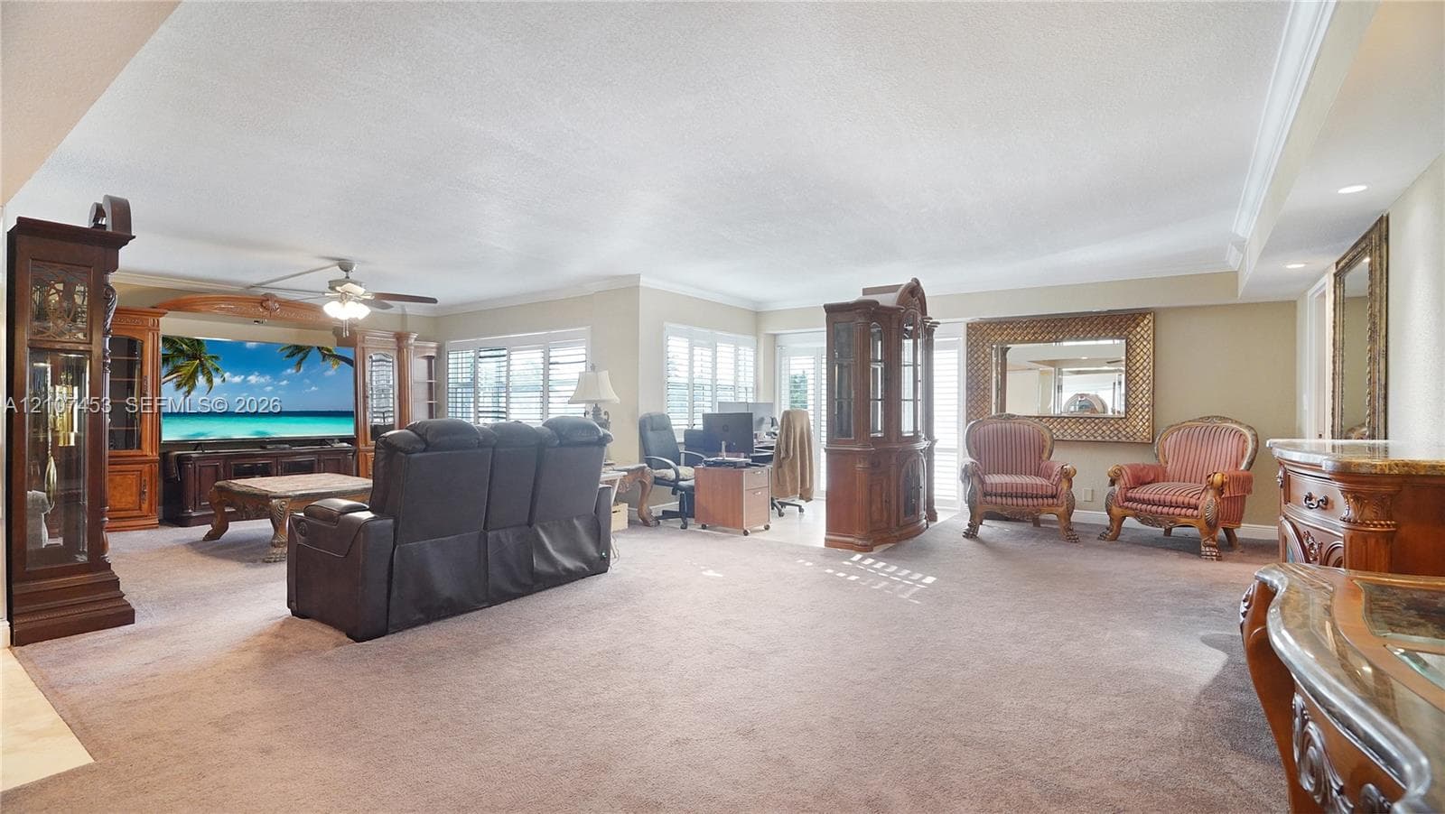 Expansive living area featuring custom built-in wood cabinetry, integrated ceiling fan, and multi-pane windows with shutters