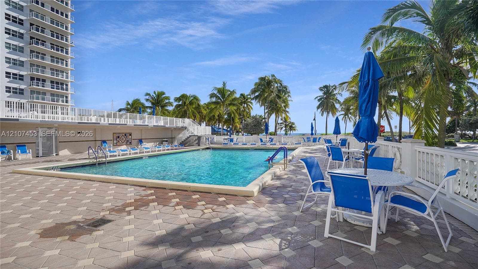 Swimming pool with a paved deck, white balustrade fencing, and mature palm trees