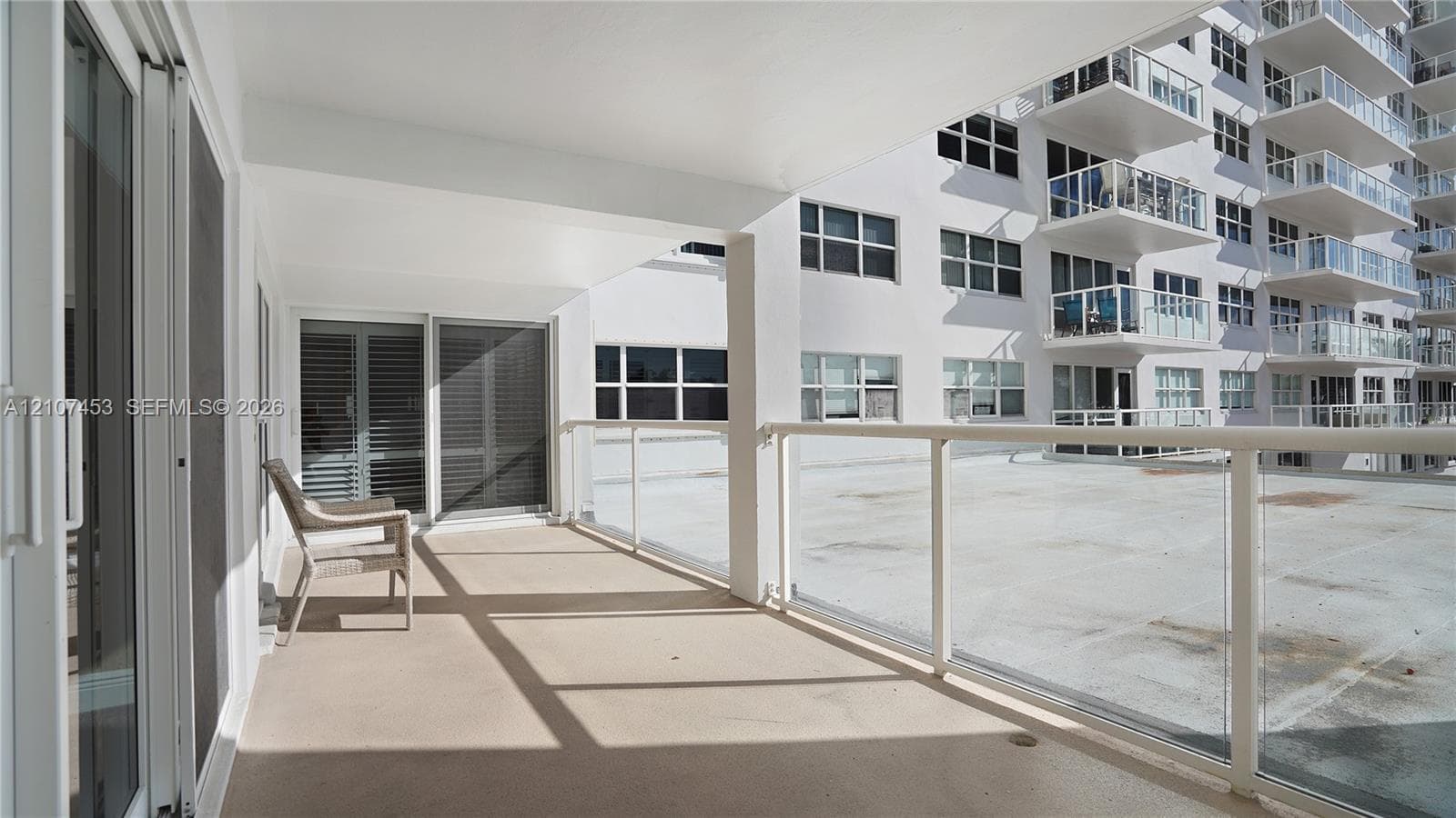Covered balcony featuring glass pane railings, solid-surface flooring, and sliding glass door access