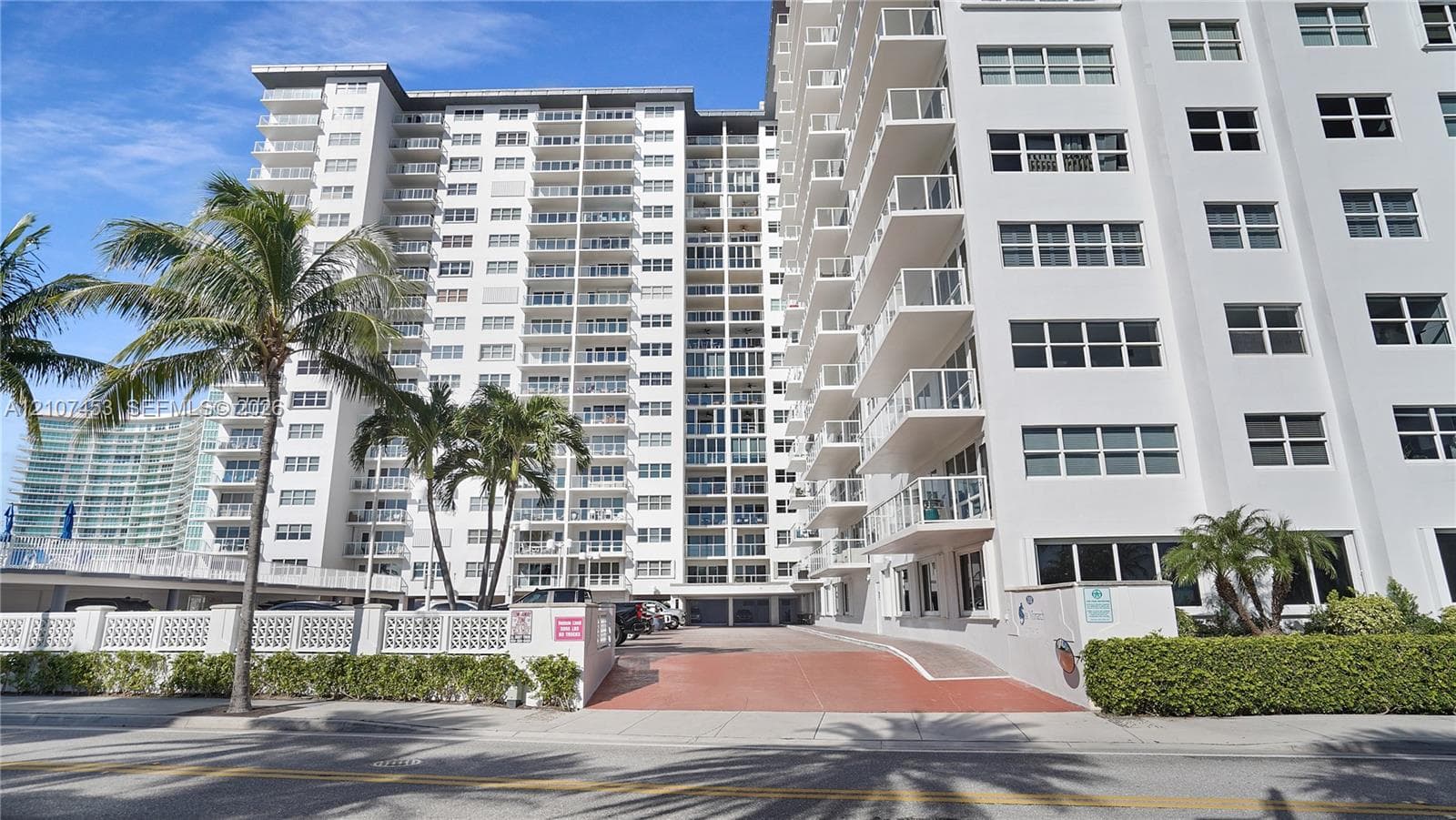 Multi-story high-rise exterior featuring a reinforced concrete facade, private balconies with glass railings, and ground-level paved parking
