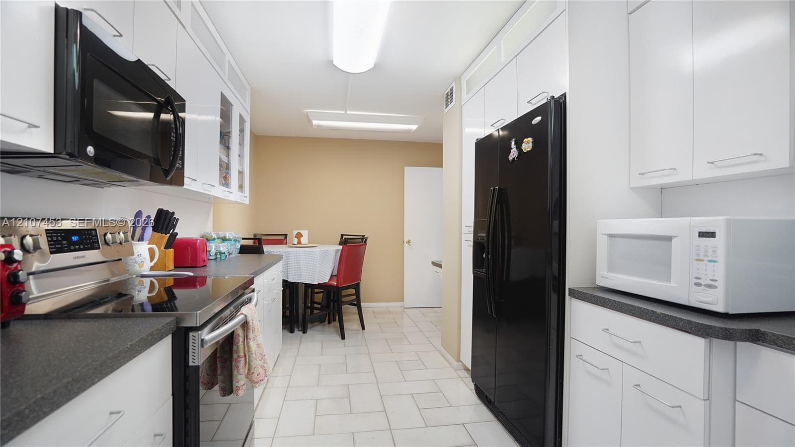 Galley kitchen featuring white cabinetry, dark countertops, tile flooring, and integrated appliances