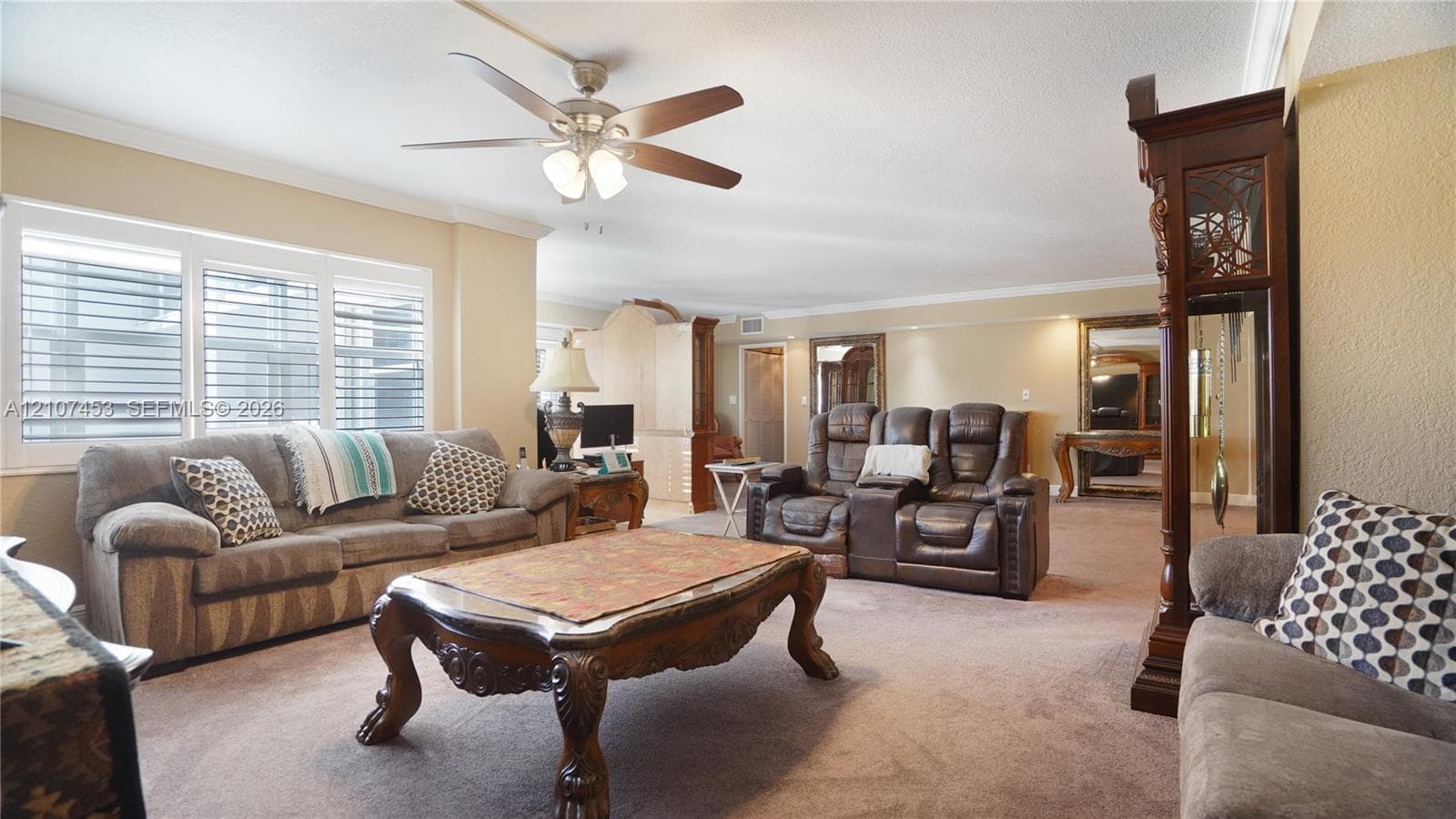 Spacious living area featuring neutral wall tones, large window assembly with integrated shutters, and a ceiling-mounted fan with light fixture