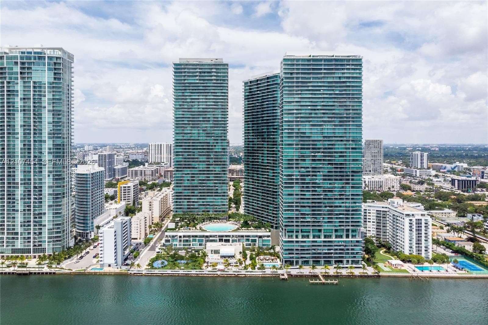 High-rise complex featuring glass-facade towers, an elevated outdoor pool, landscaped podium deck, and direct waterfront placement