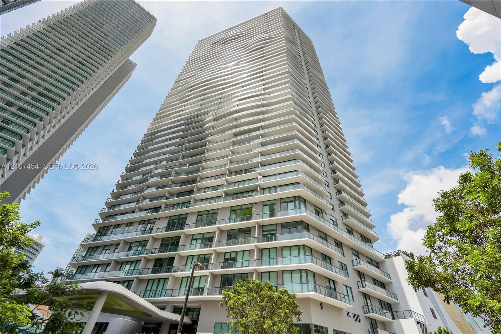 High-rise tower exterior featuring a multi-story facade, cantilevered balconies with glass railings, large-pane windows, and a structured concrete architectural design